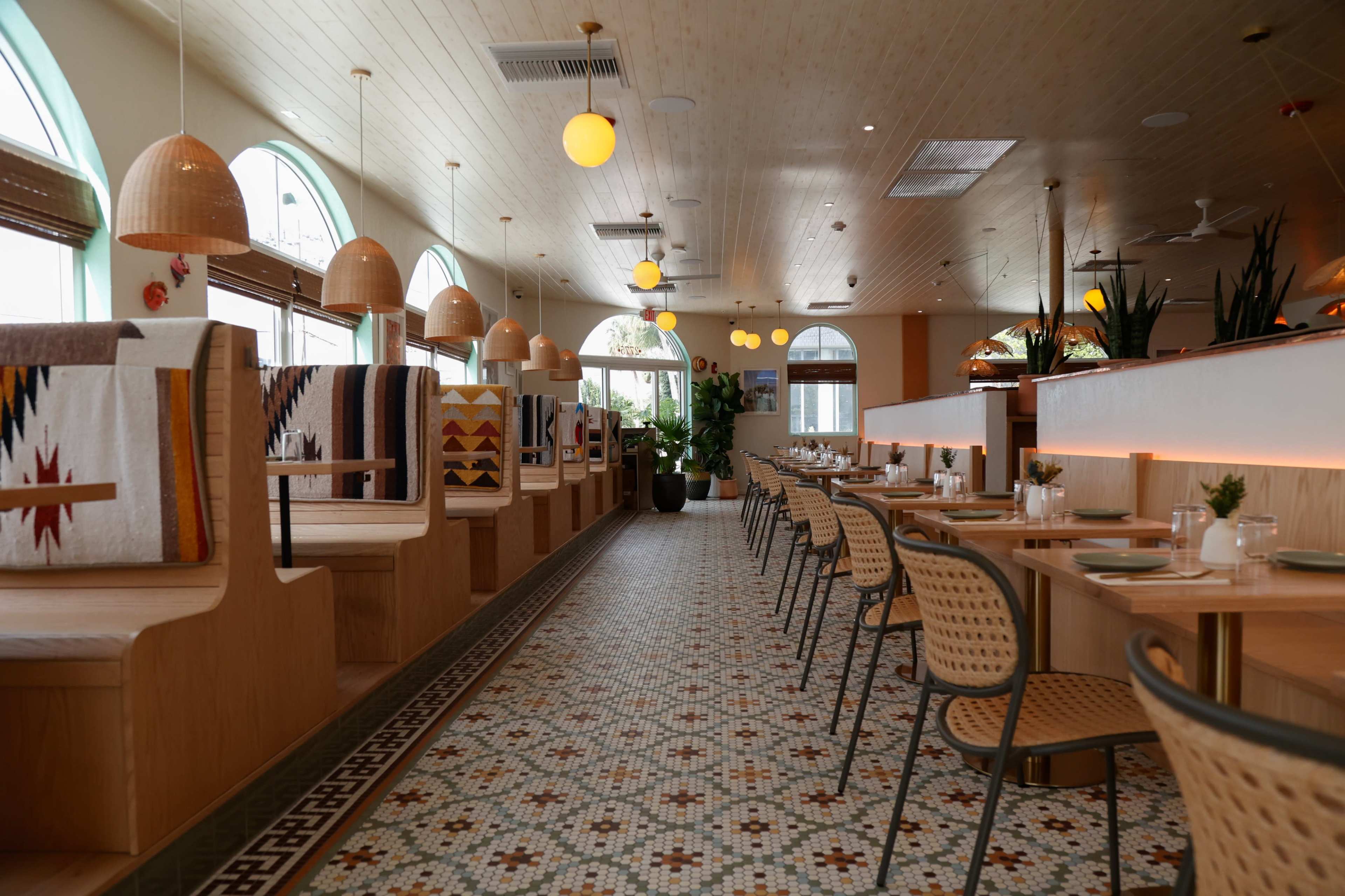 The image shows a brightly lit, modern restaurant interior with wooden booths, patterned tiles, and stylish pendant lights.