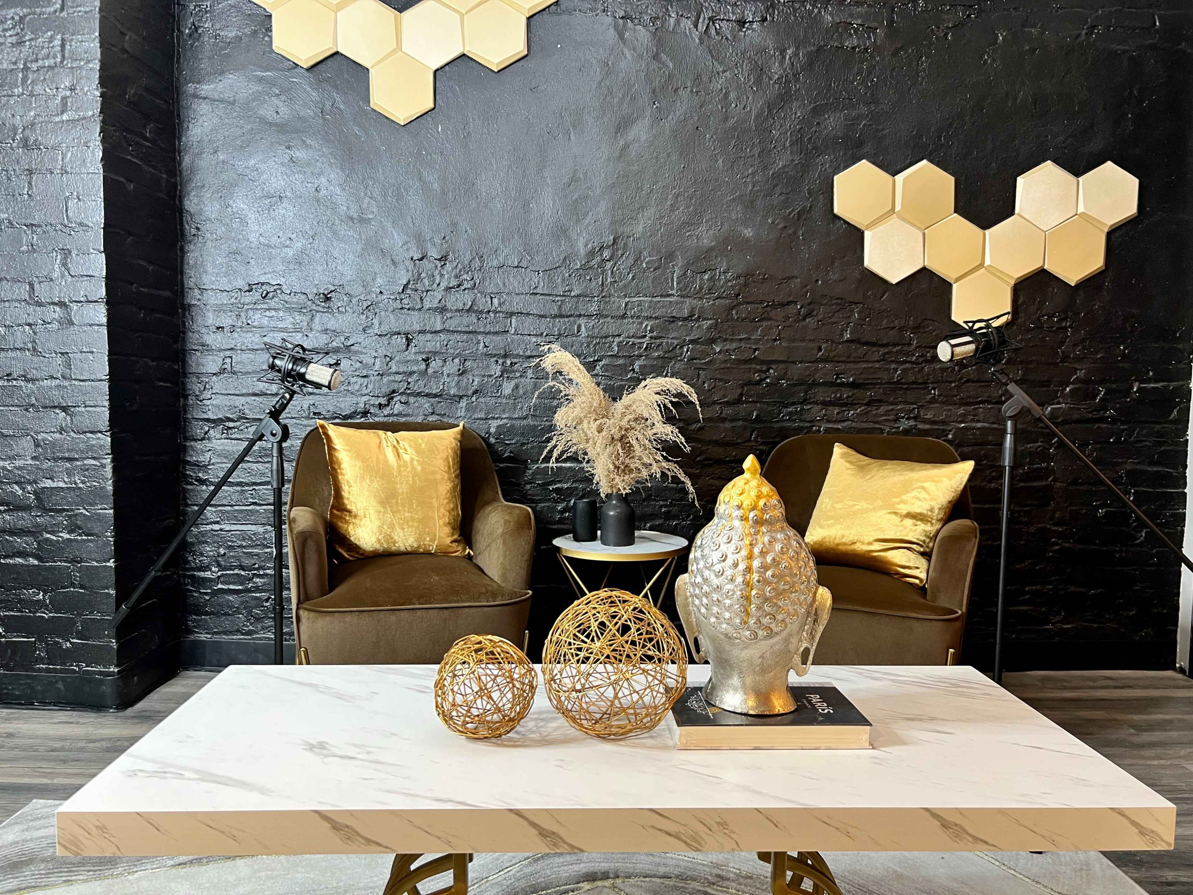 The scene features two velvet armchairs with gold cushions flanking a marble coffee table, adorned with decorative spheres and a buddha statue, against a backdrop of a black brick wall with geometric accents.