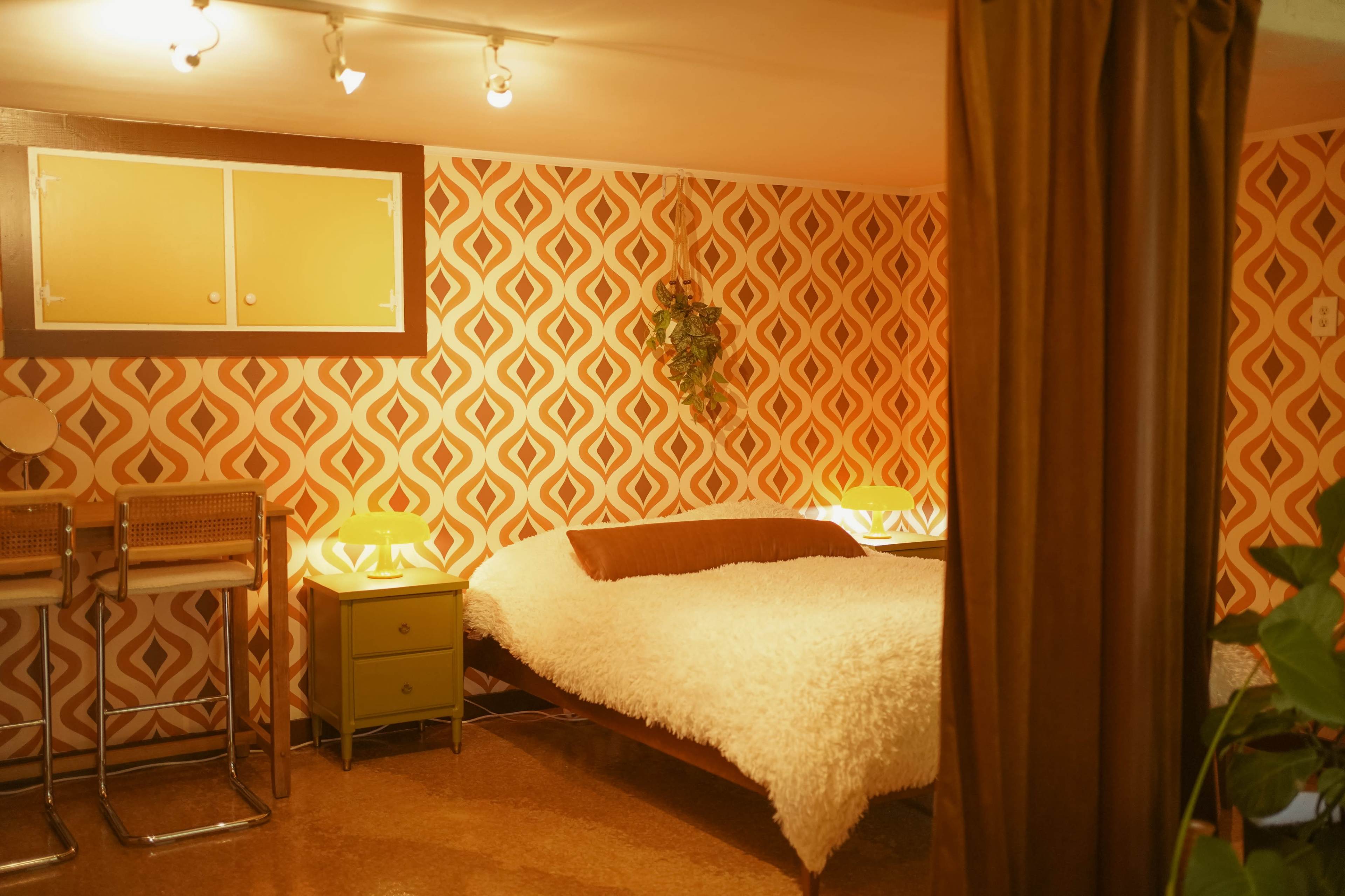 A bedroom with a patterned orange wallpaper, a bed covered in a white throw, and two bedside tables with lamps.