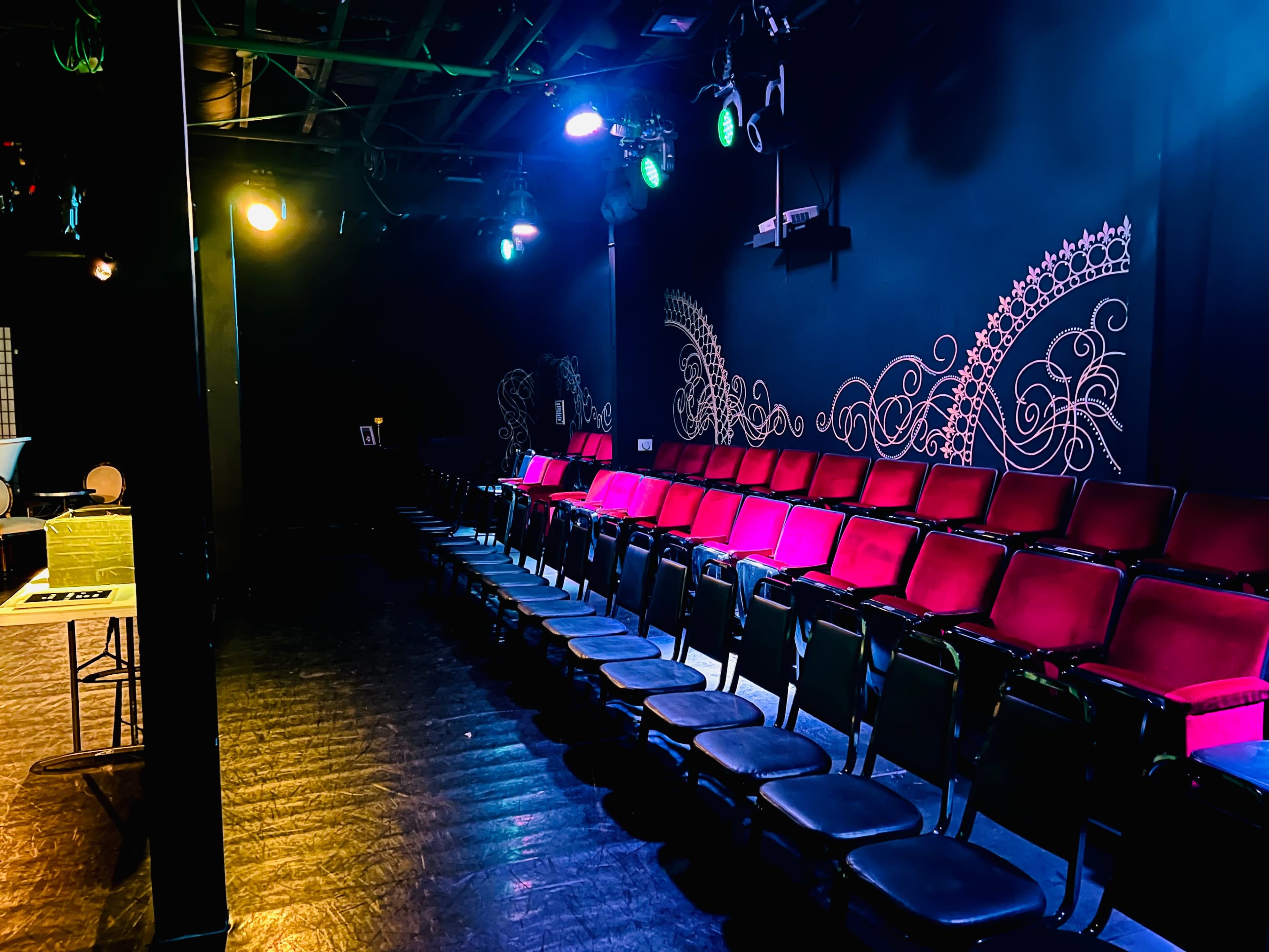 A dimly lit theater features a row of red and black seats against a black wall decorated with intricate designs.