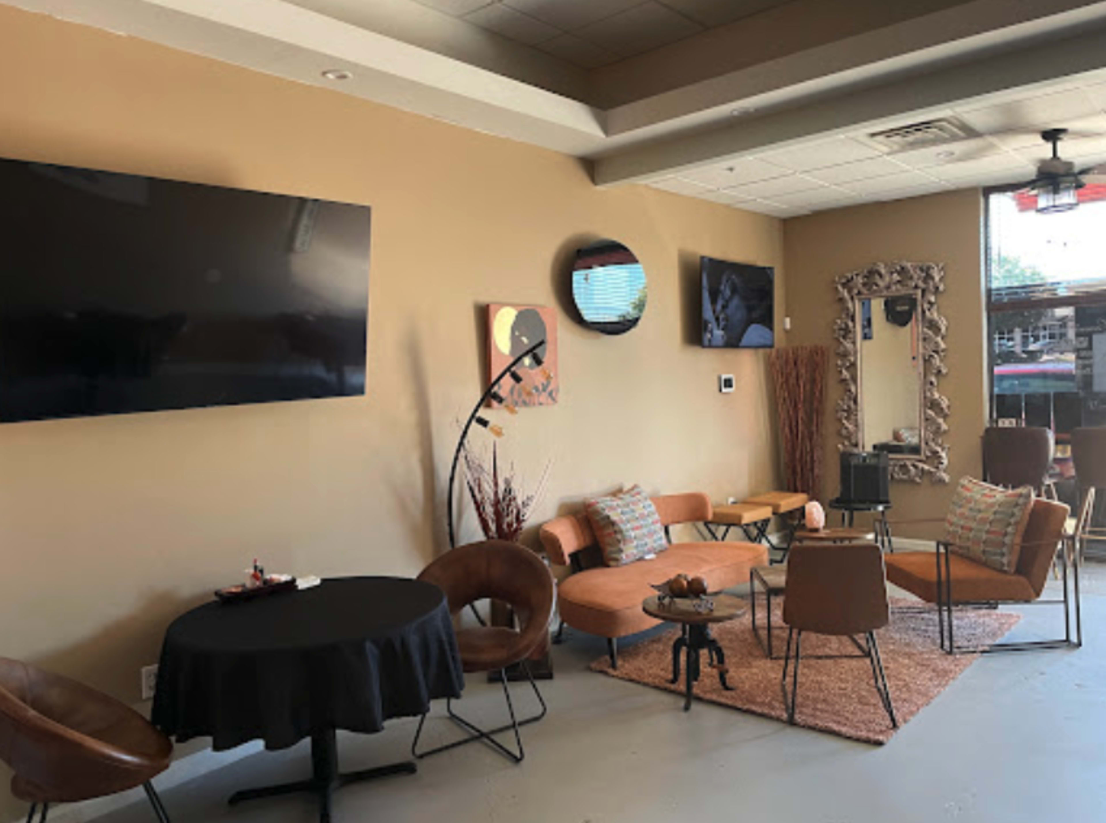 A modern lounge area with multiple seating options, including a round table and various chairs, along with two large wall-mounted TVs.