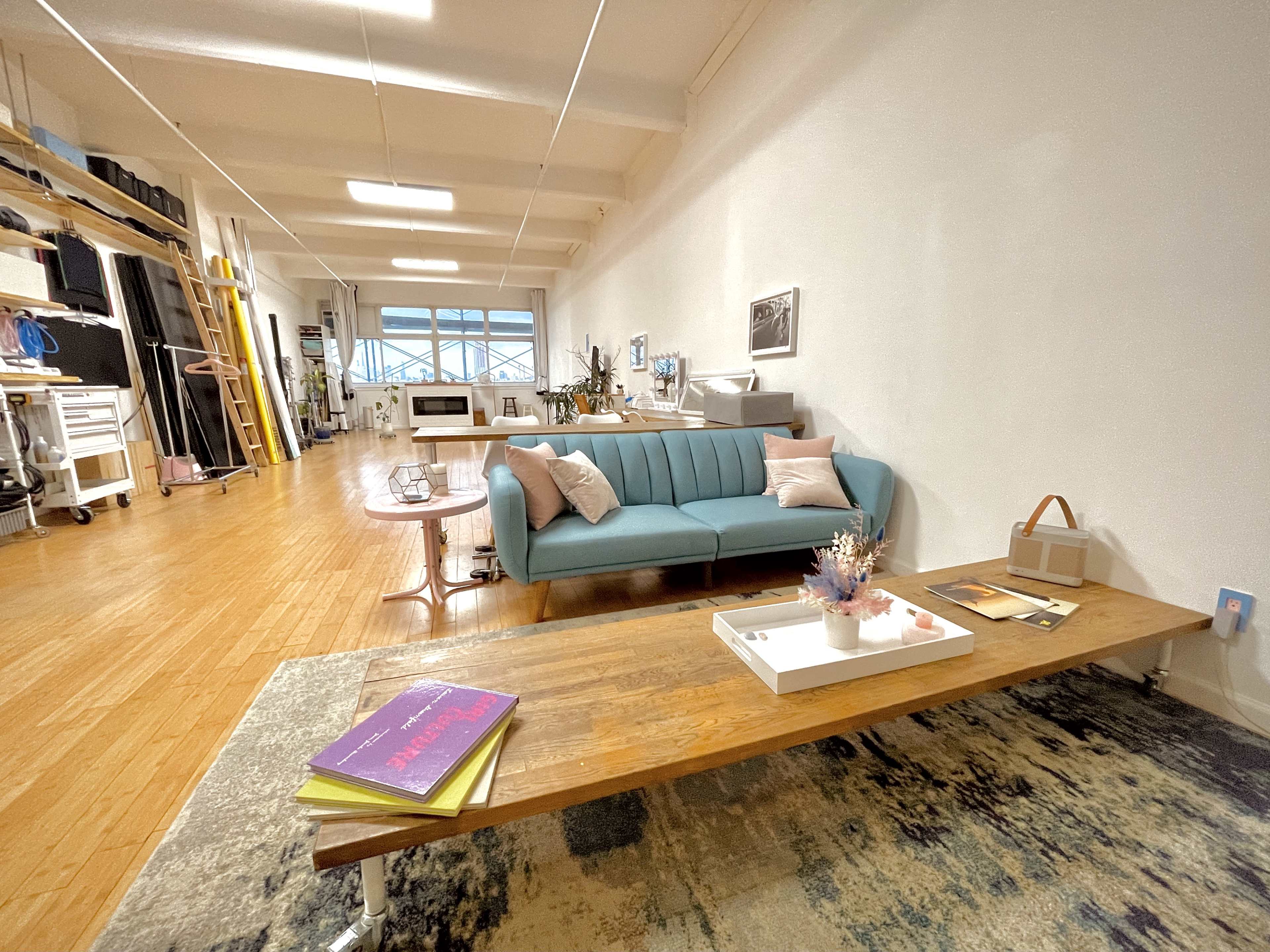 A spacious room featuring a light blue couch, a wooden coffee table with books, and a variety of furniture and decor items in a bright, well-lit environment.