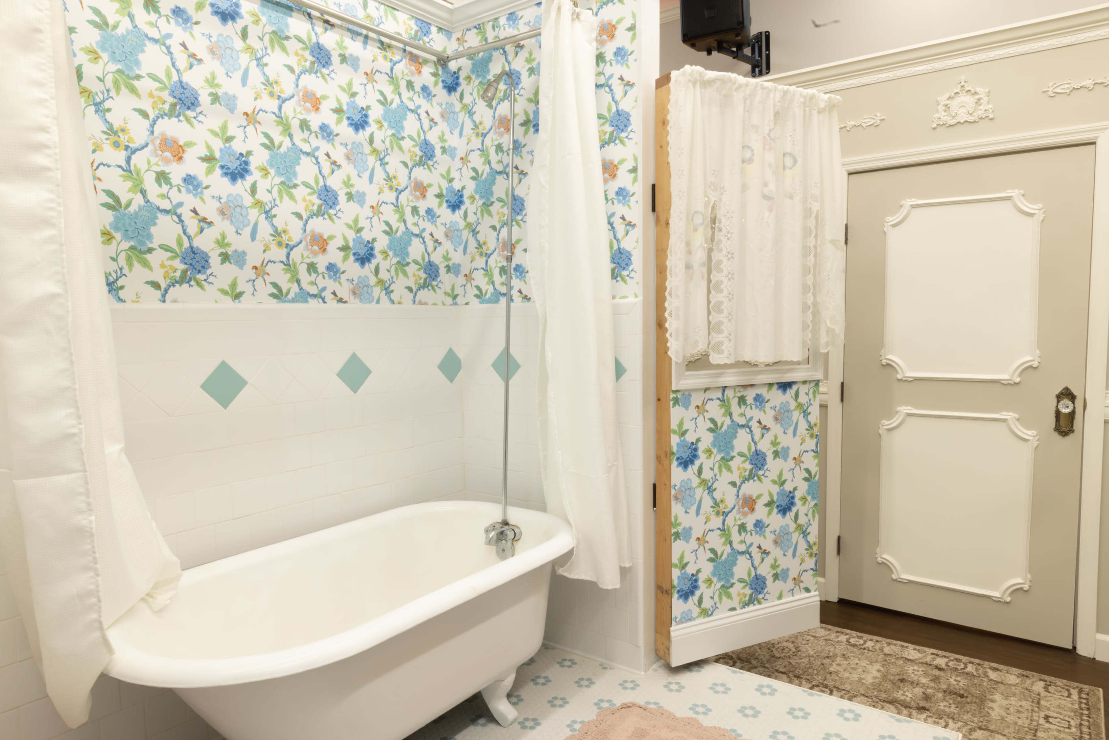 A bathroom featuring a clawfoot bathtub, floral wallpaper, and a door with decorative trim.