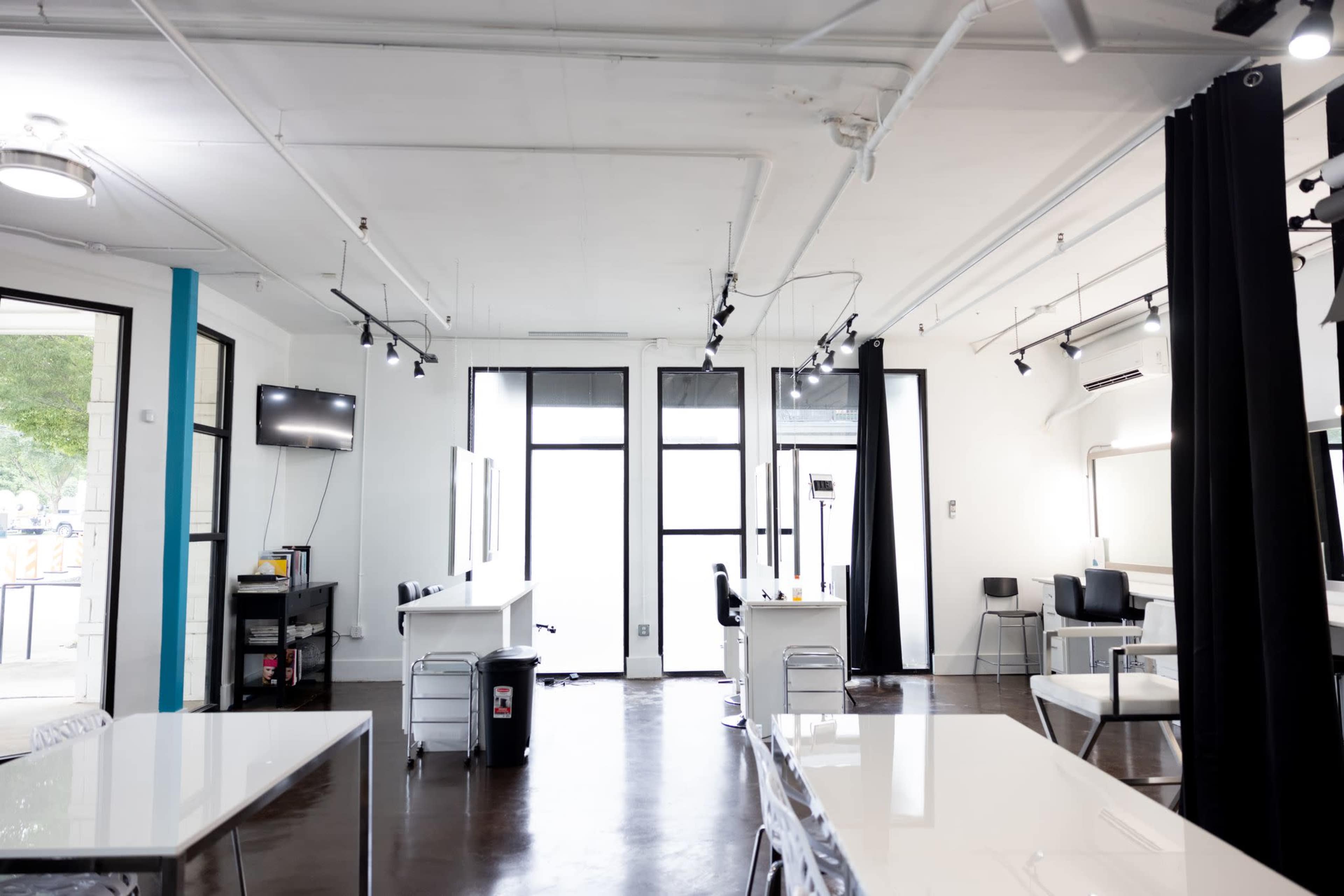 The image shows a spacious, modern salon interior with multiple styling stations, large windows, and minimalist decor.