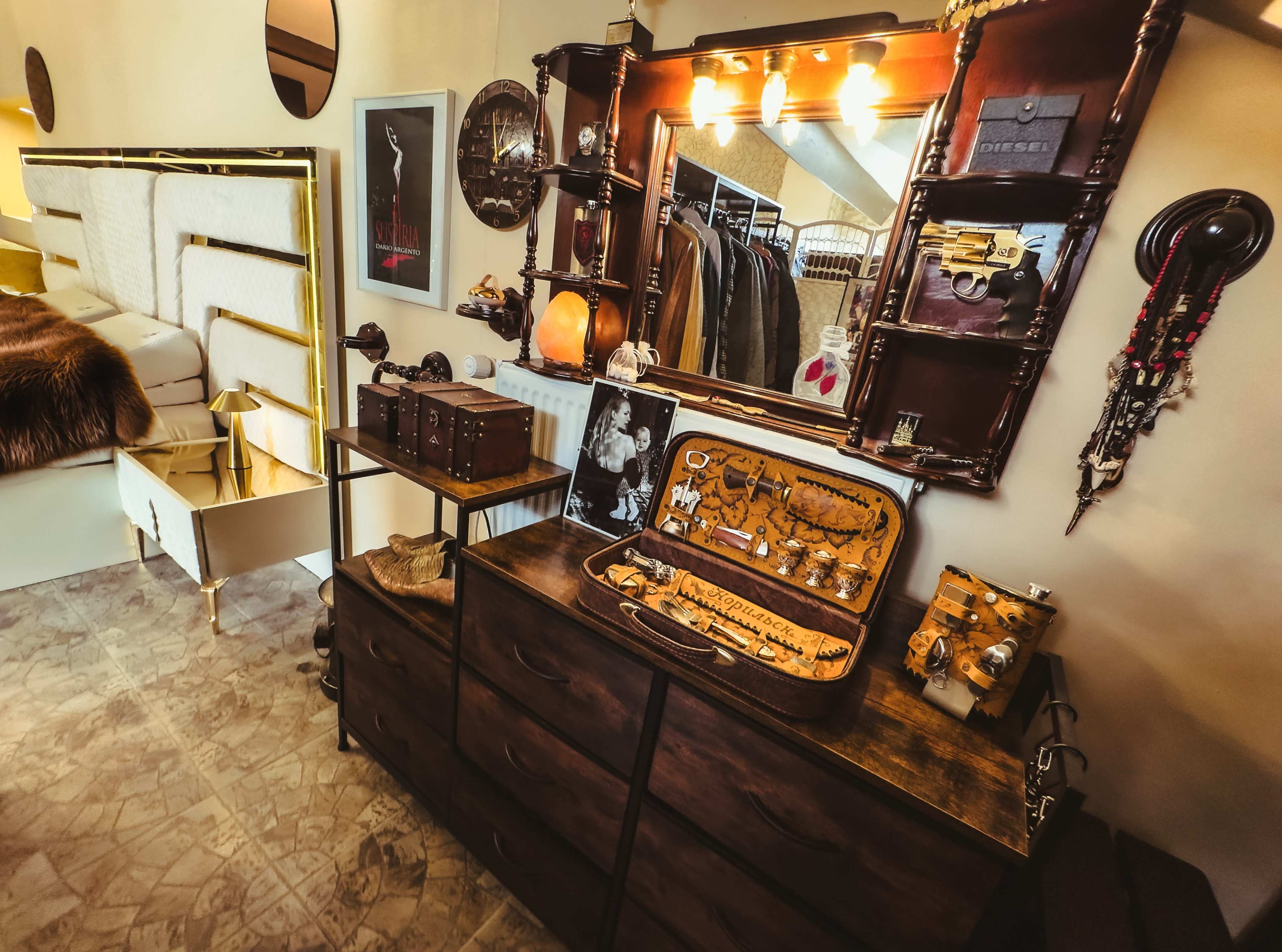 The image shows a well-organized bedroom with a wooden dresser displaying various jewelry items, a mirror with lights above it, and a wardrobe in the background.
