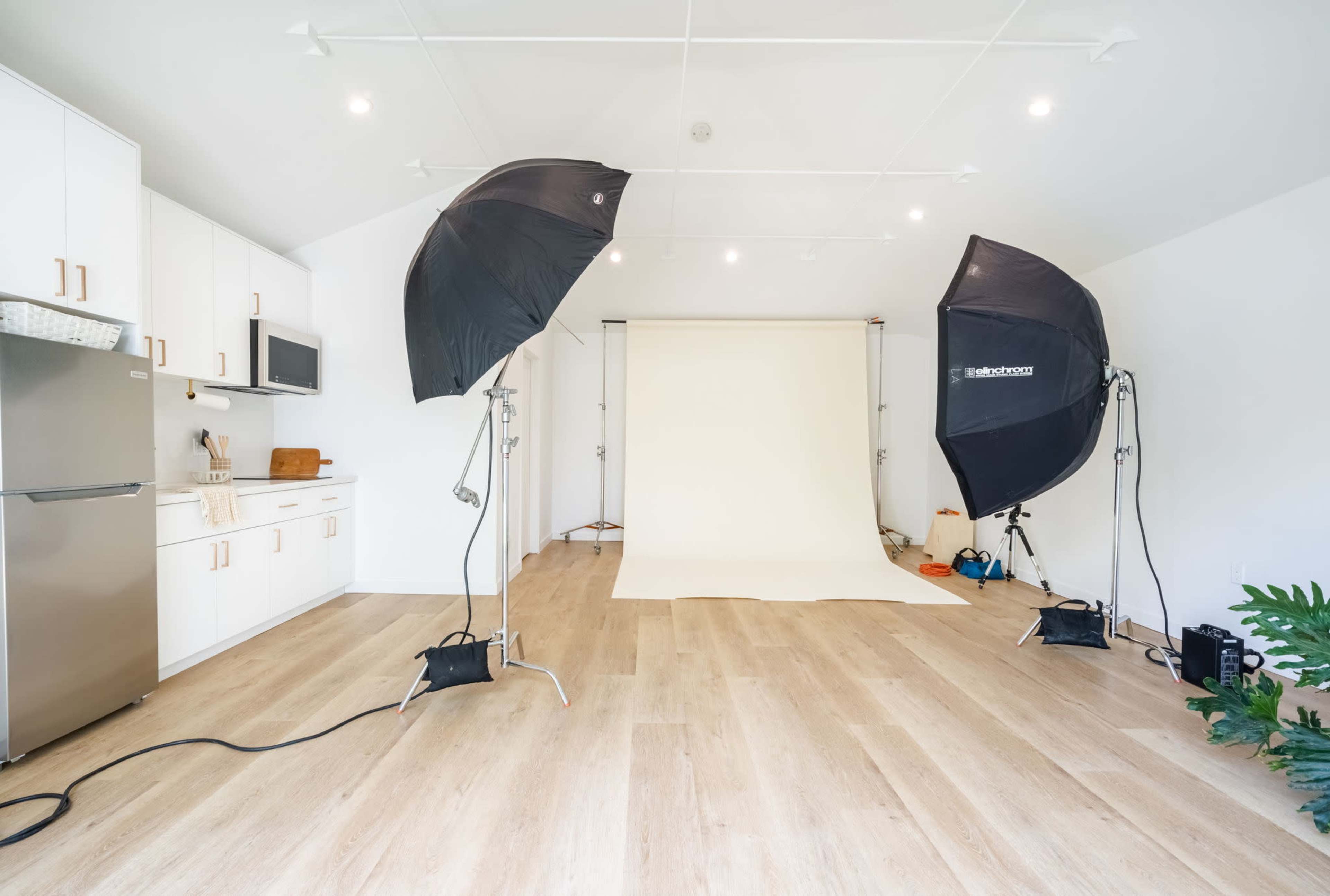 A photography studio equipped with softbox lights, a neutral backdrop, and kitchen amenities in the background.