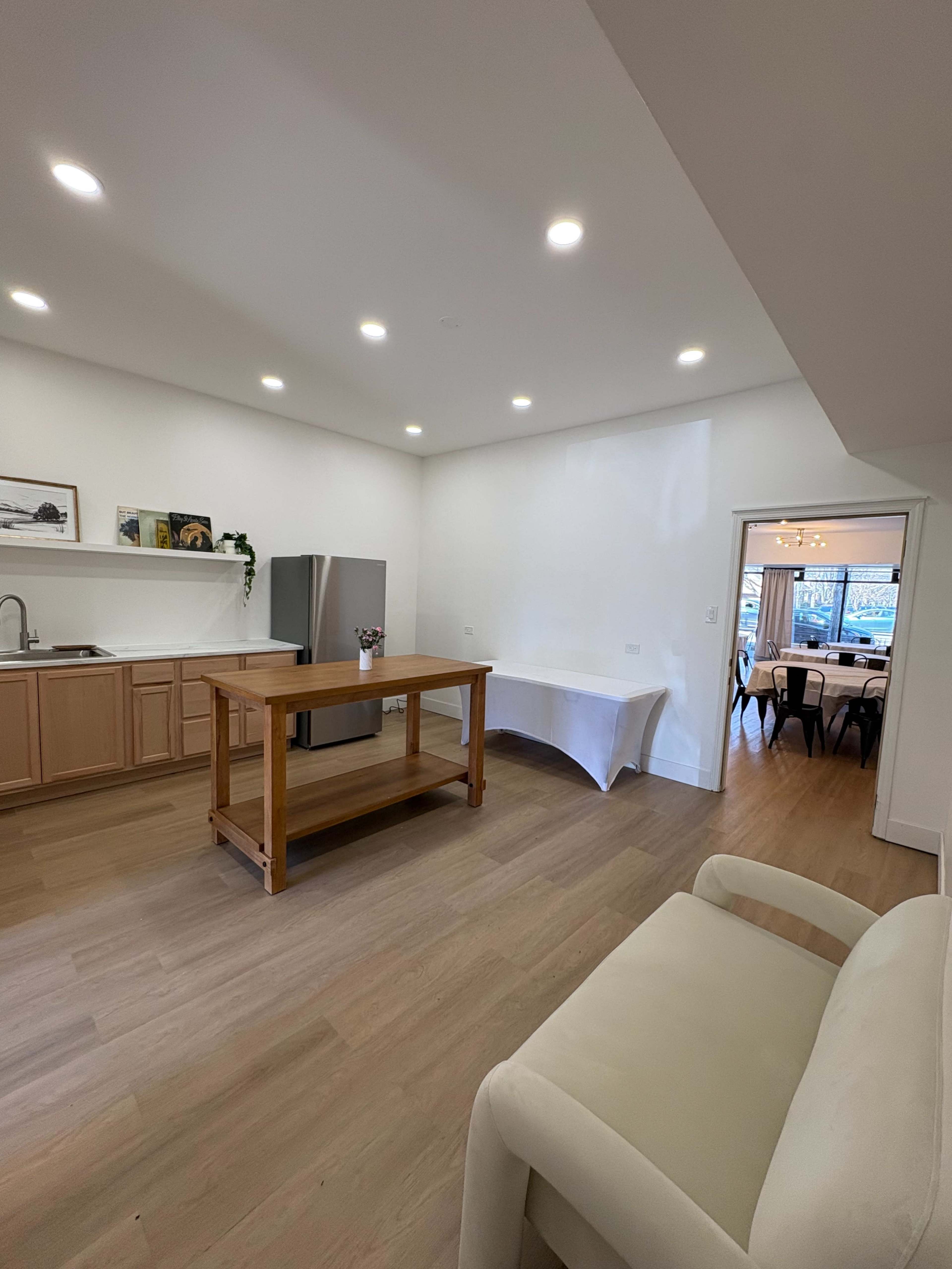The image shows a spacious, modern kitchen with wooden cabinetry, a large island in the center, and a dining area visible through an open doorway.