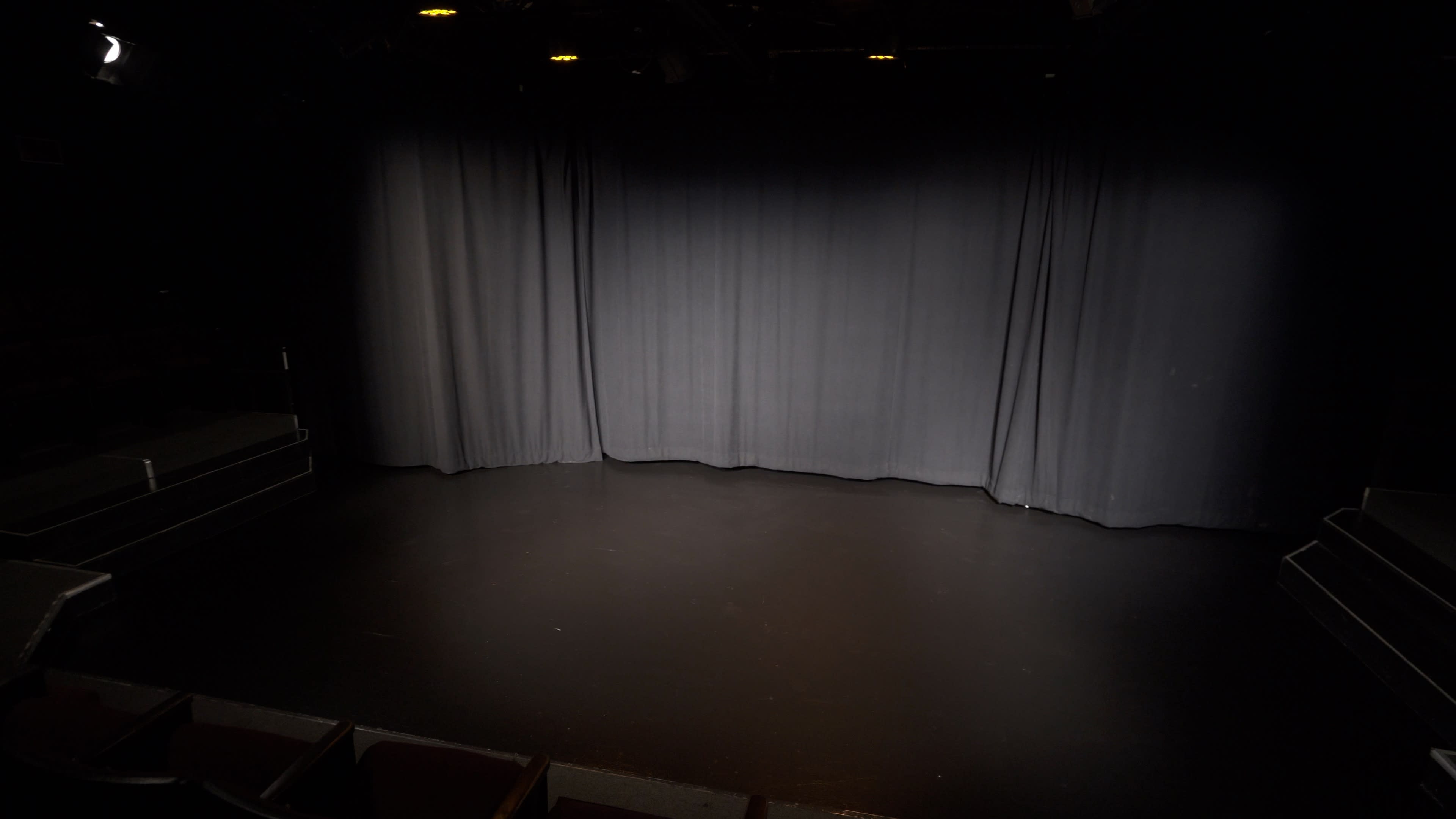 A darkened theater stage with black curtains drawn closed, set on a smooth black floor.