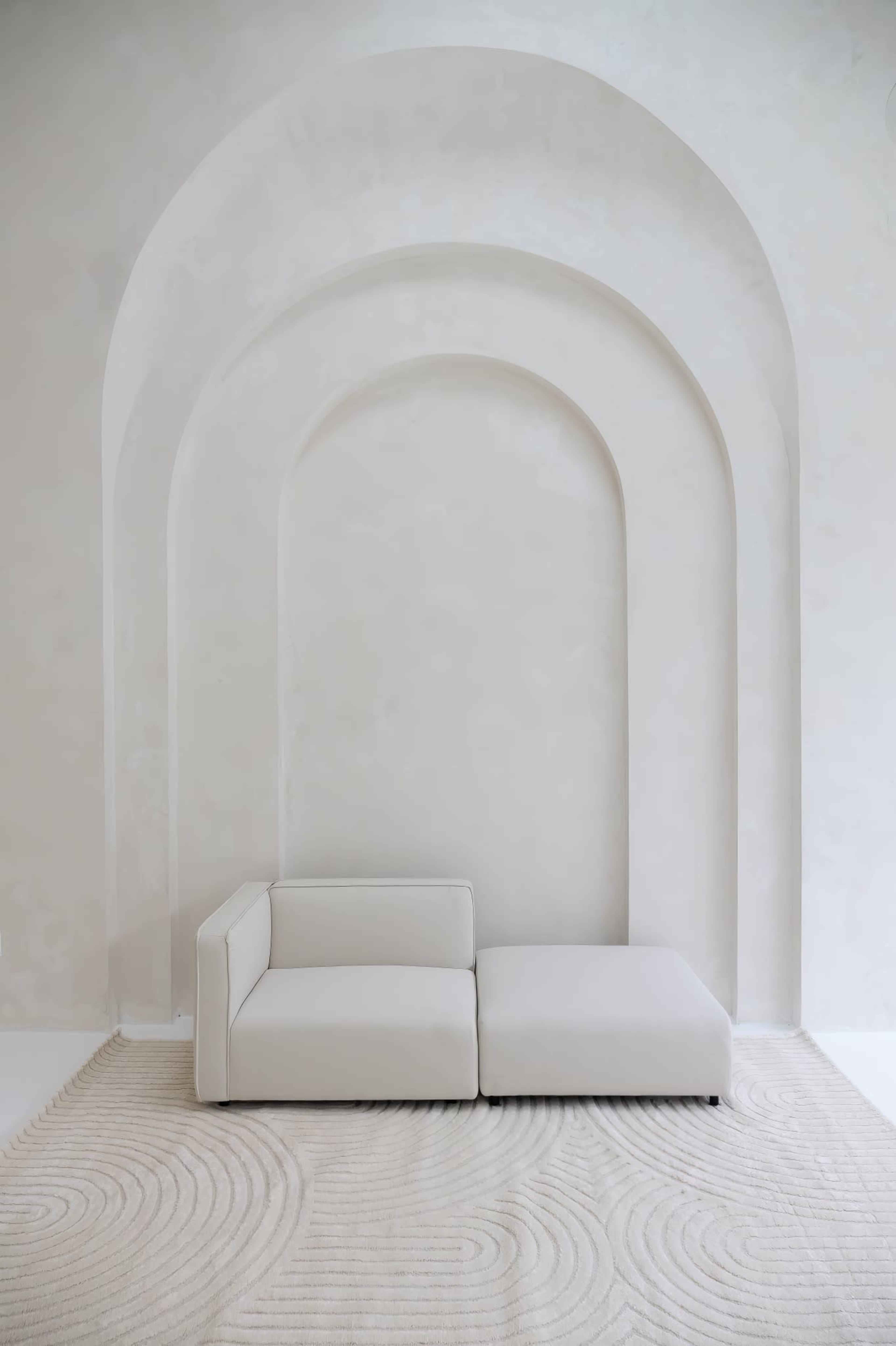 A white sectional sofa is positioned against a light-colored, arch-shaped wall with a textured finish.