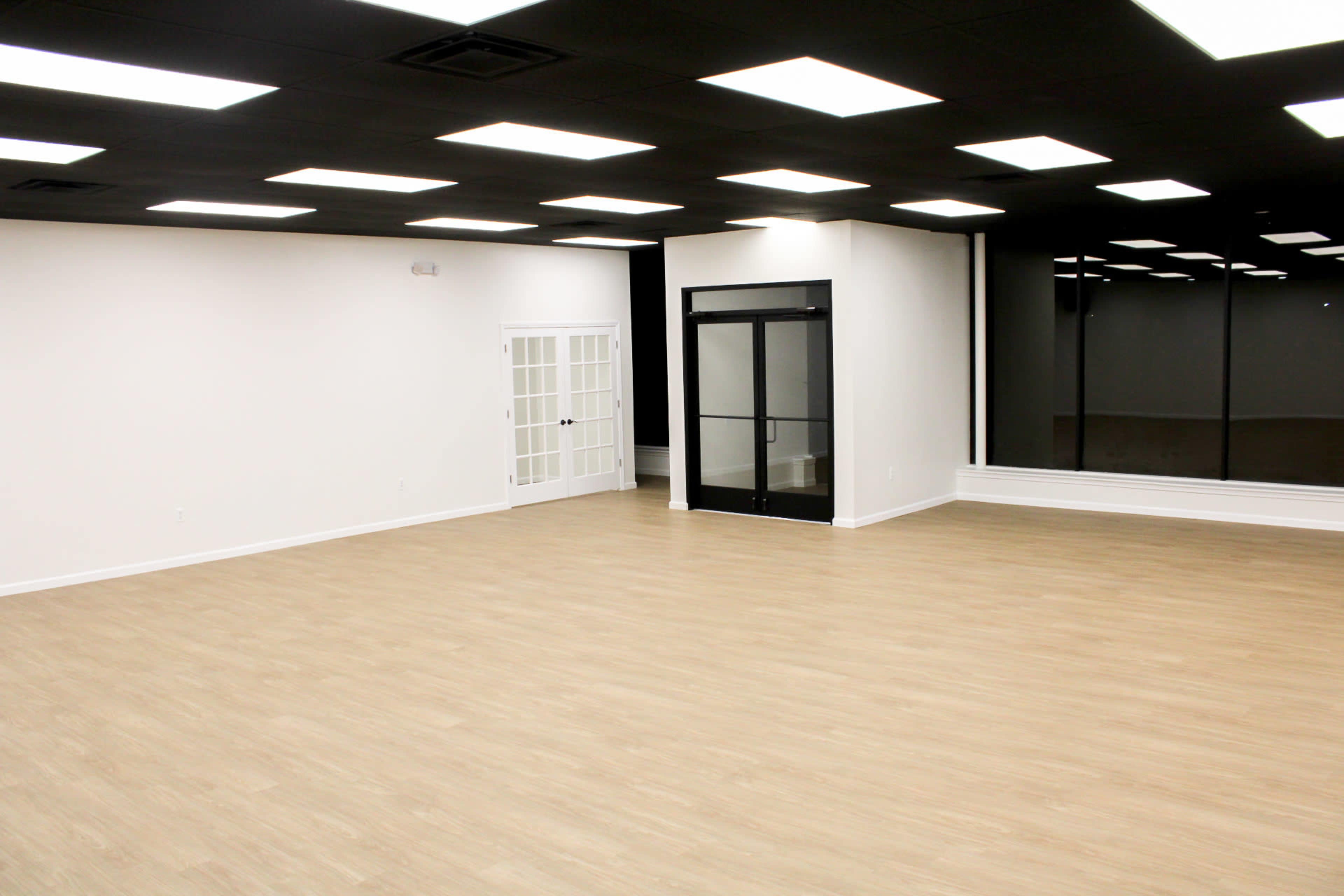 The image shows a spacious, empty room with light-colored flooring, white walls, and a large glass window.
