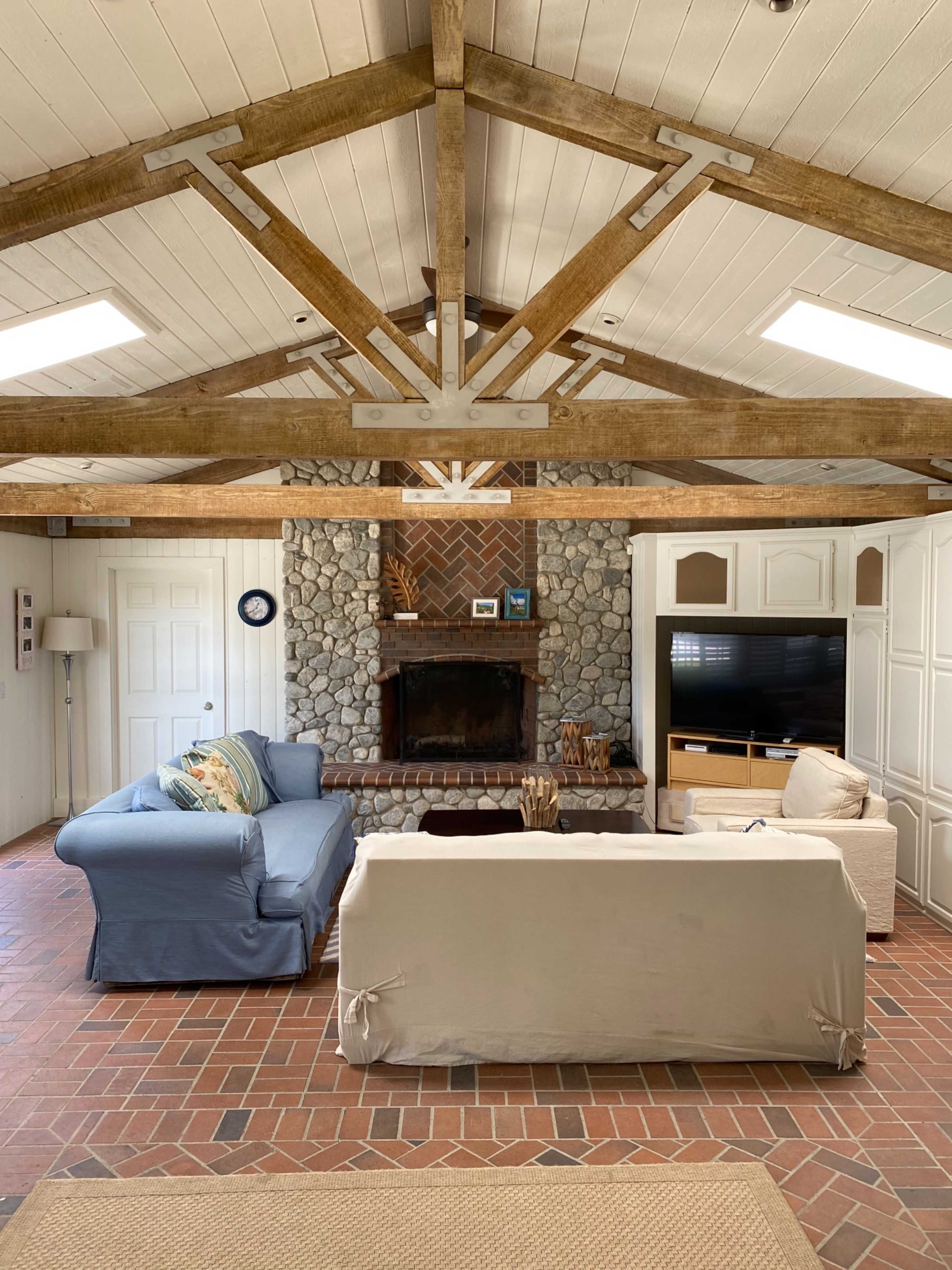 A spacious living room with two sofas facing a central coffee table, a stone fireplace at the back, and wooden beams across the ceiling.