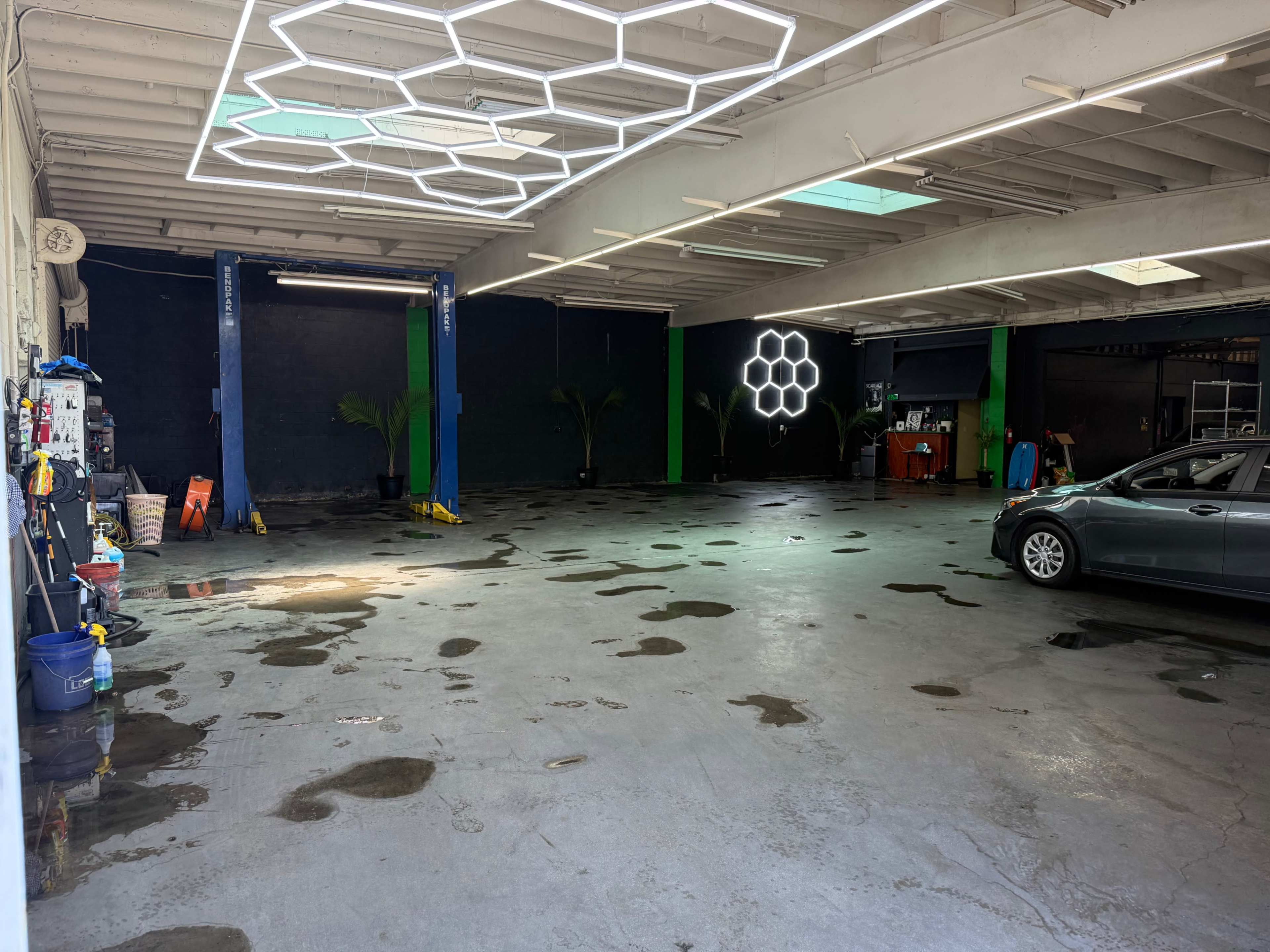 The image shows a spacious, empty garage with puddles of water on the concrete floor and brightly colored walls.