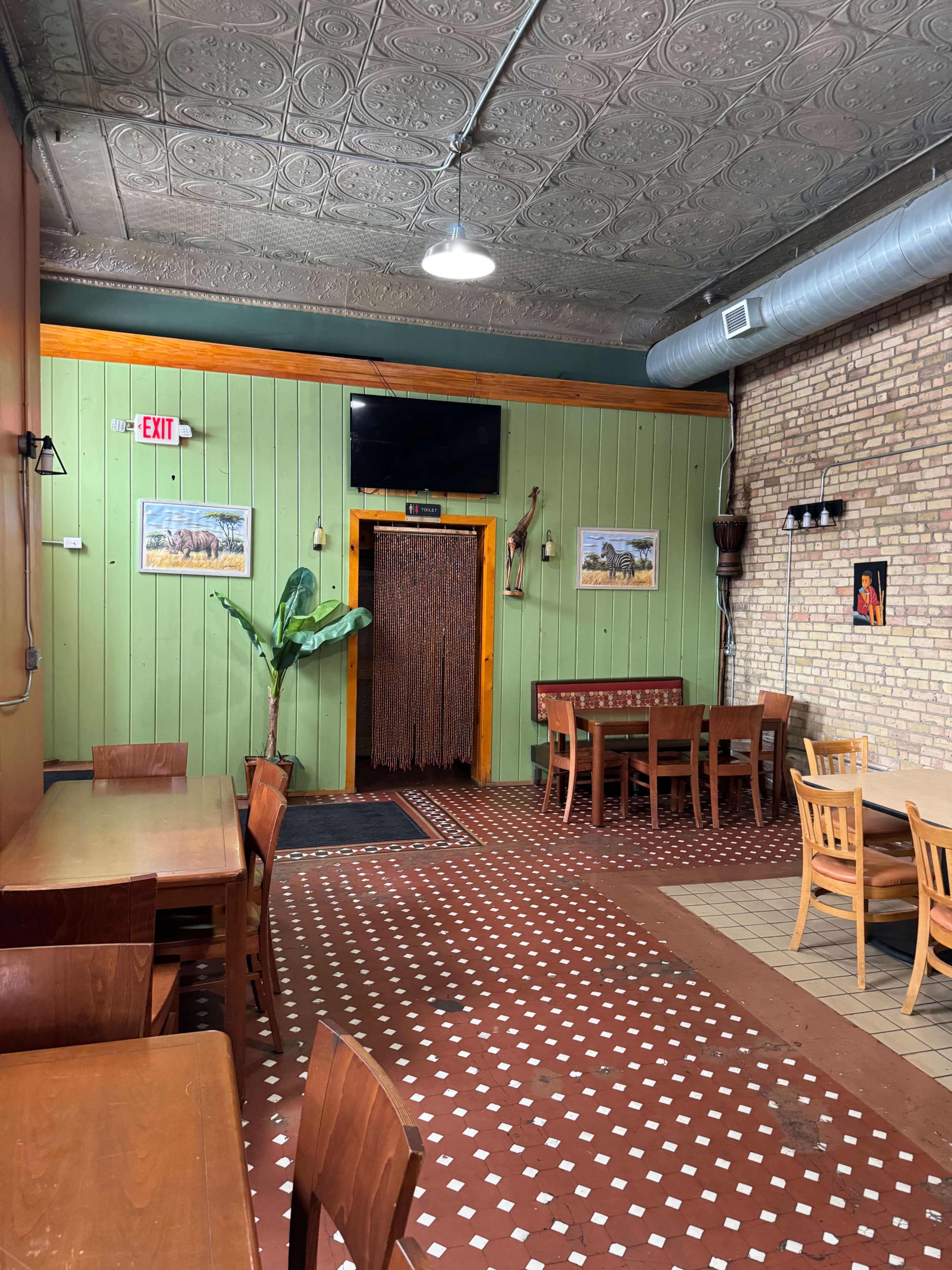 The interior of a restaurant features green walls, wooden tables and chairs, and a decorative entrance with a curtain made of strands.