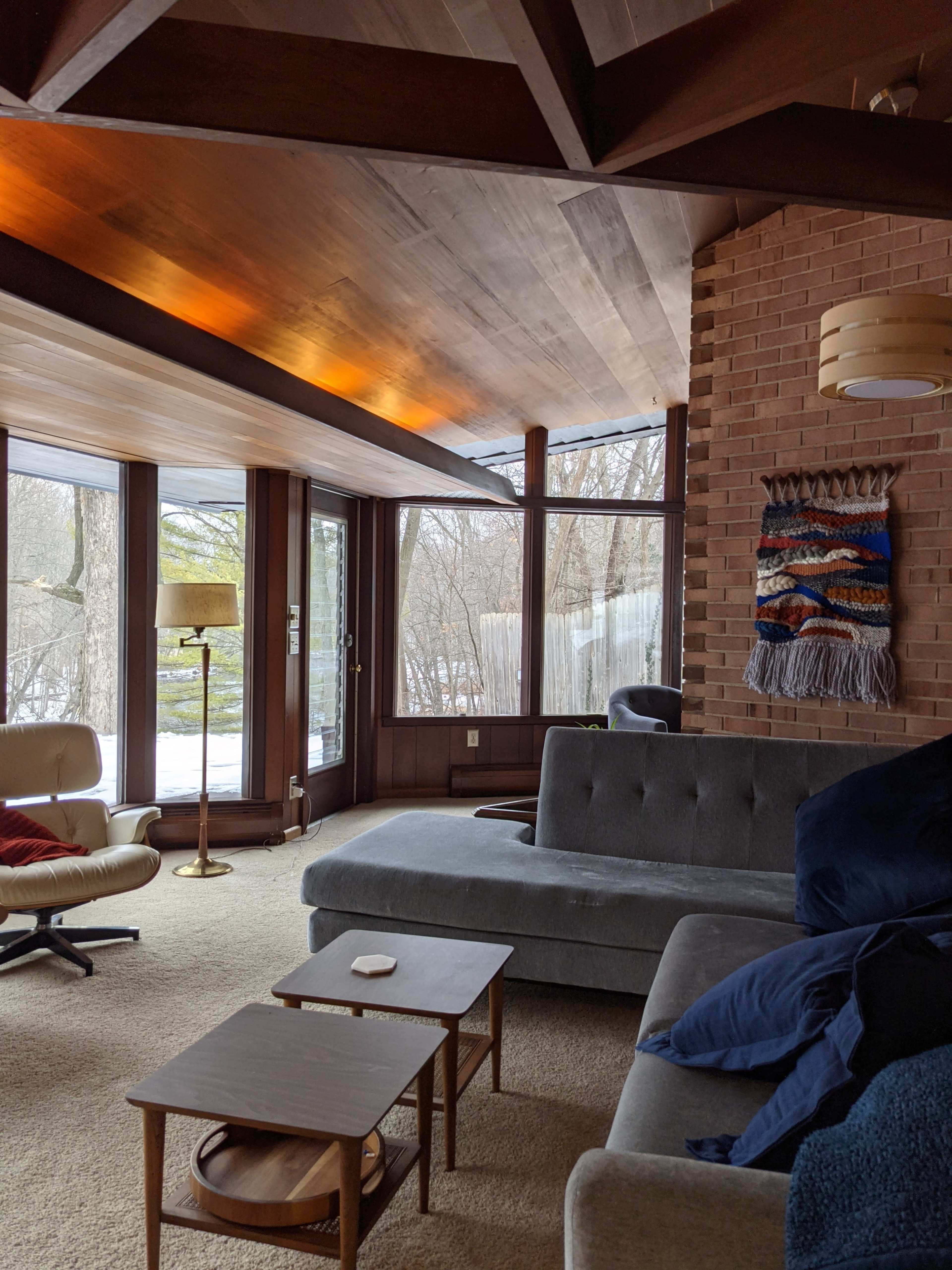 A modern living room features a gray sectional sofa, wooden coffee tables, and large windows overlooking a snowy landscape.