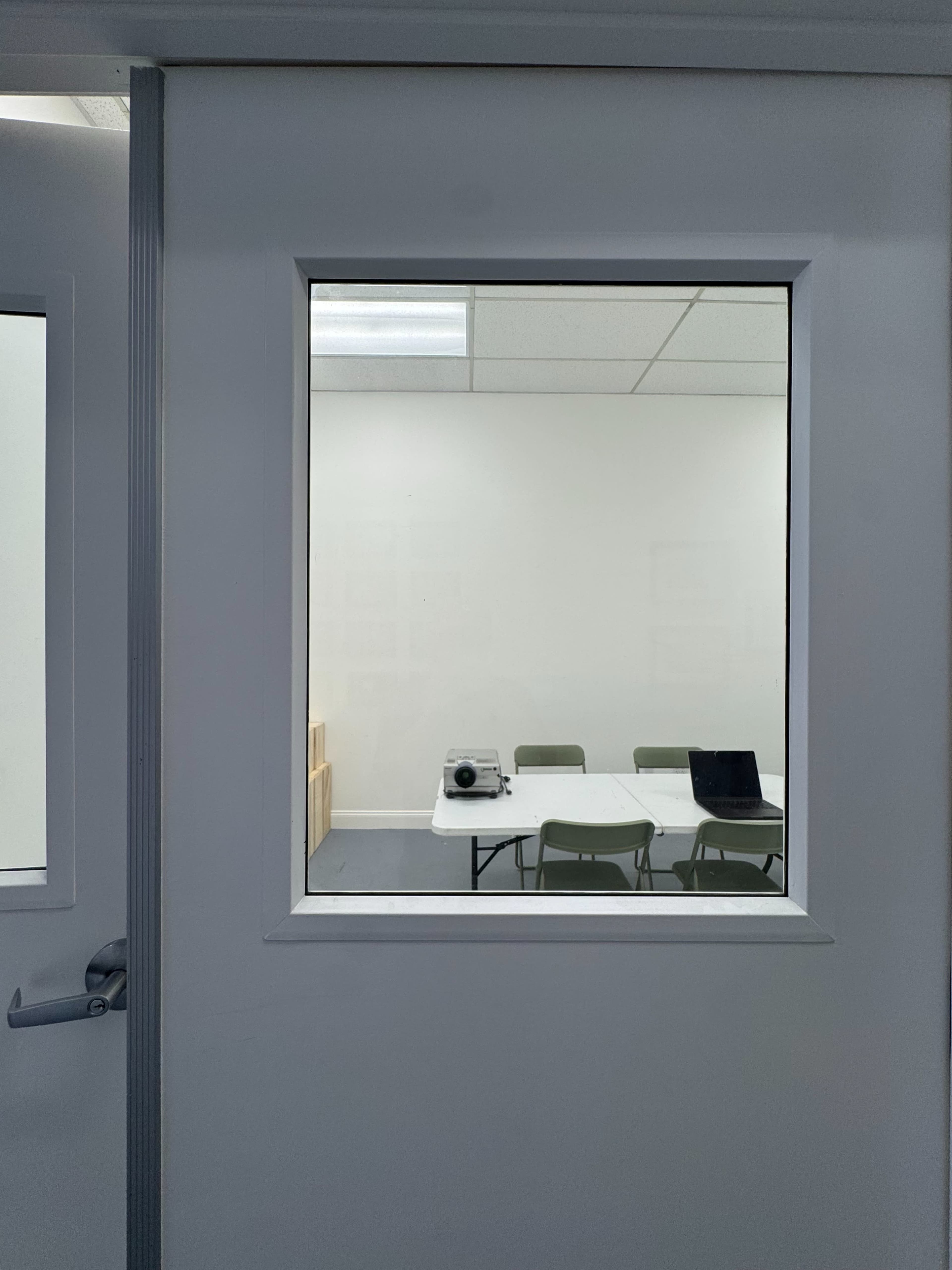 A meeting room is visible through a glass panel in a white door, featuring a table with chairs and a projector on the surface.