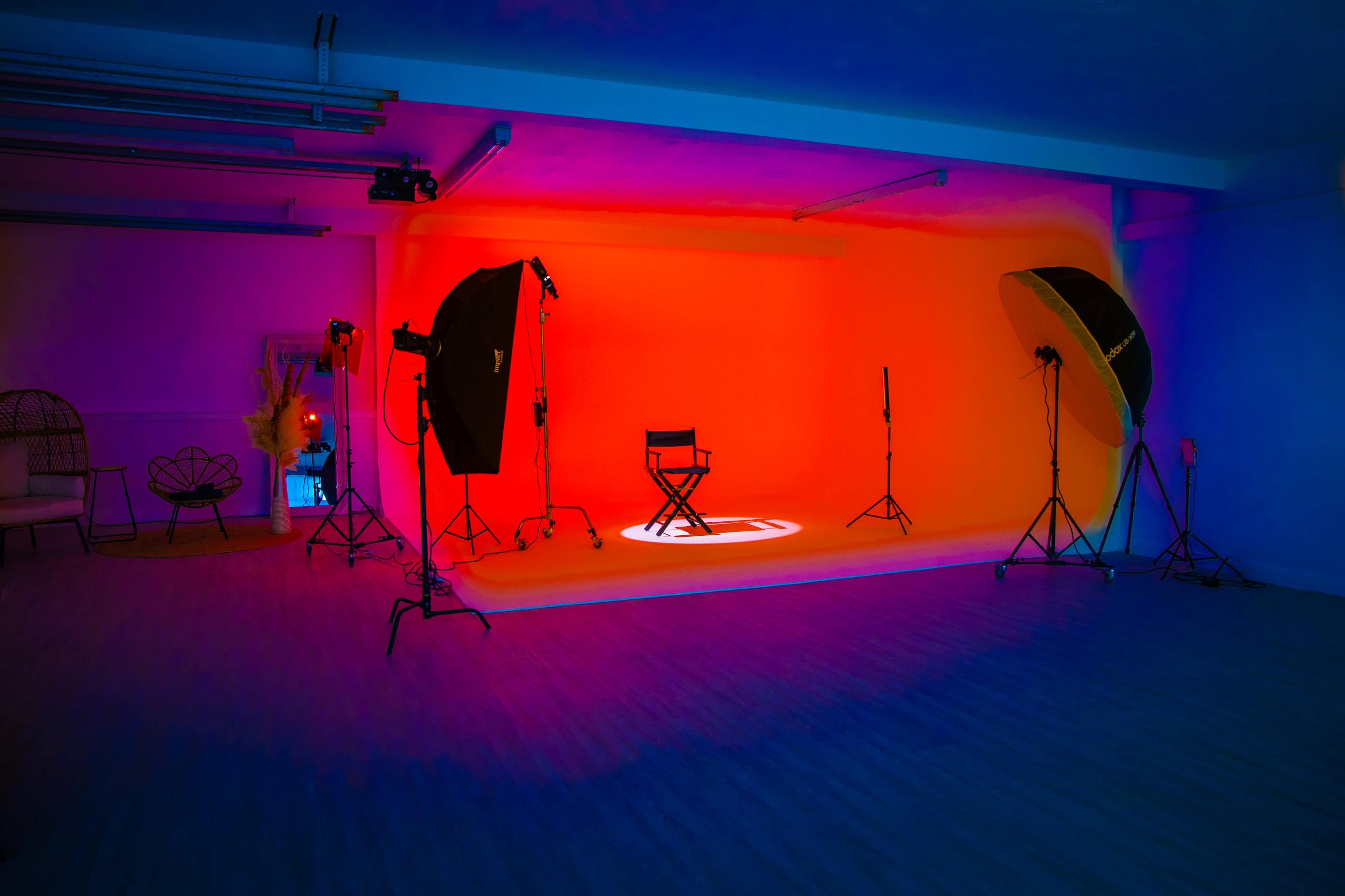 The image shows a photo studio with a brightly colored backdrop, equipped with lighting setups and a director's chair in the center.