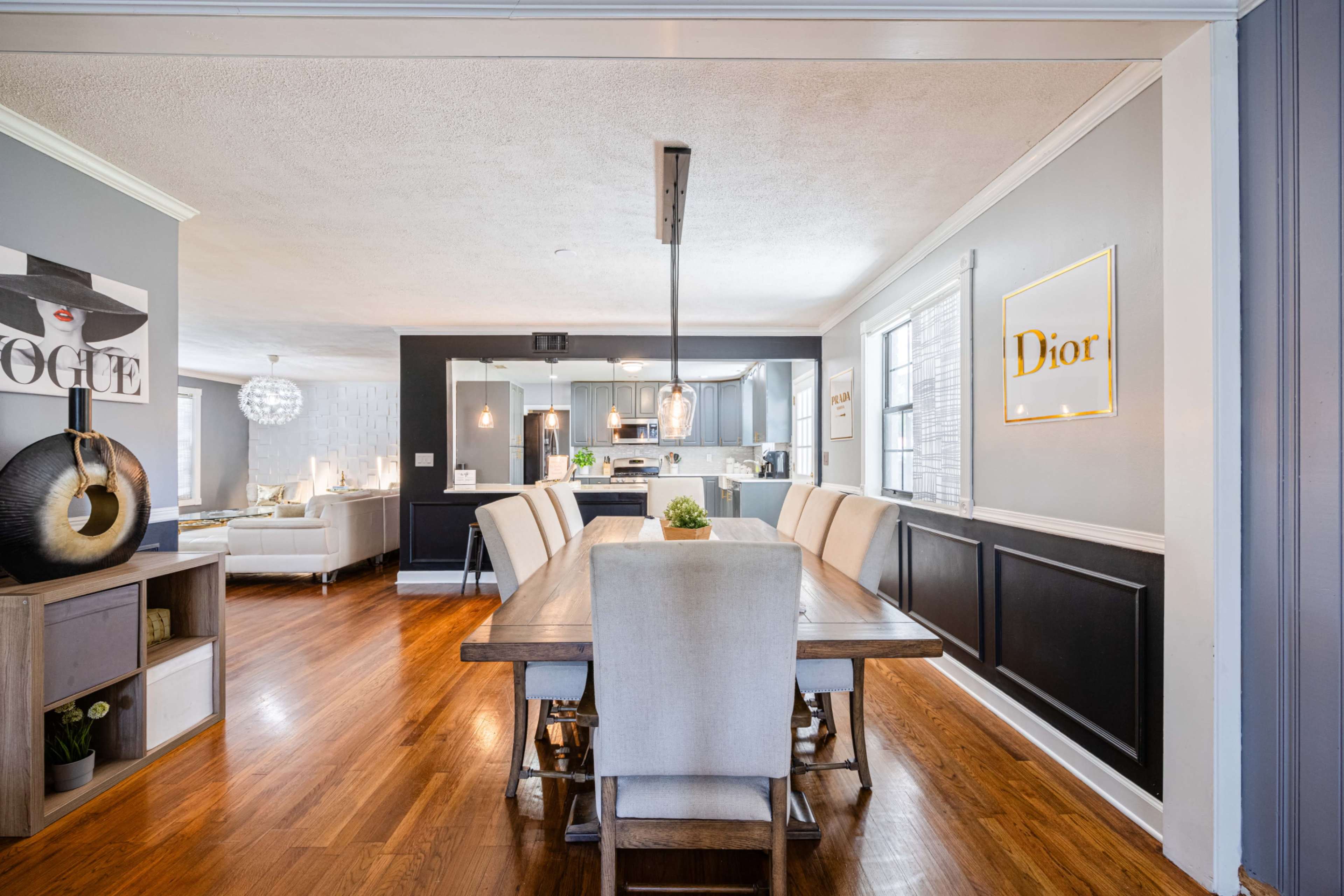 A dining area with a long table and chairs, leading into a modern kitchen and living space.
