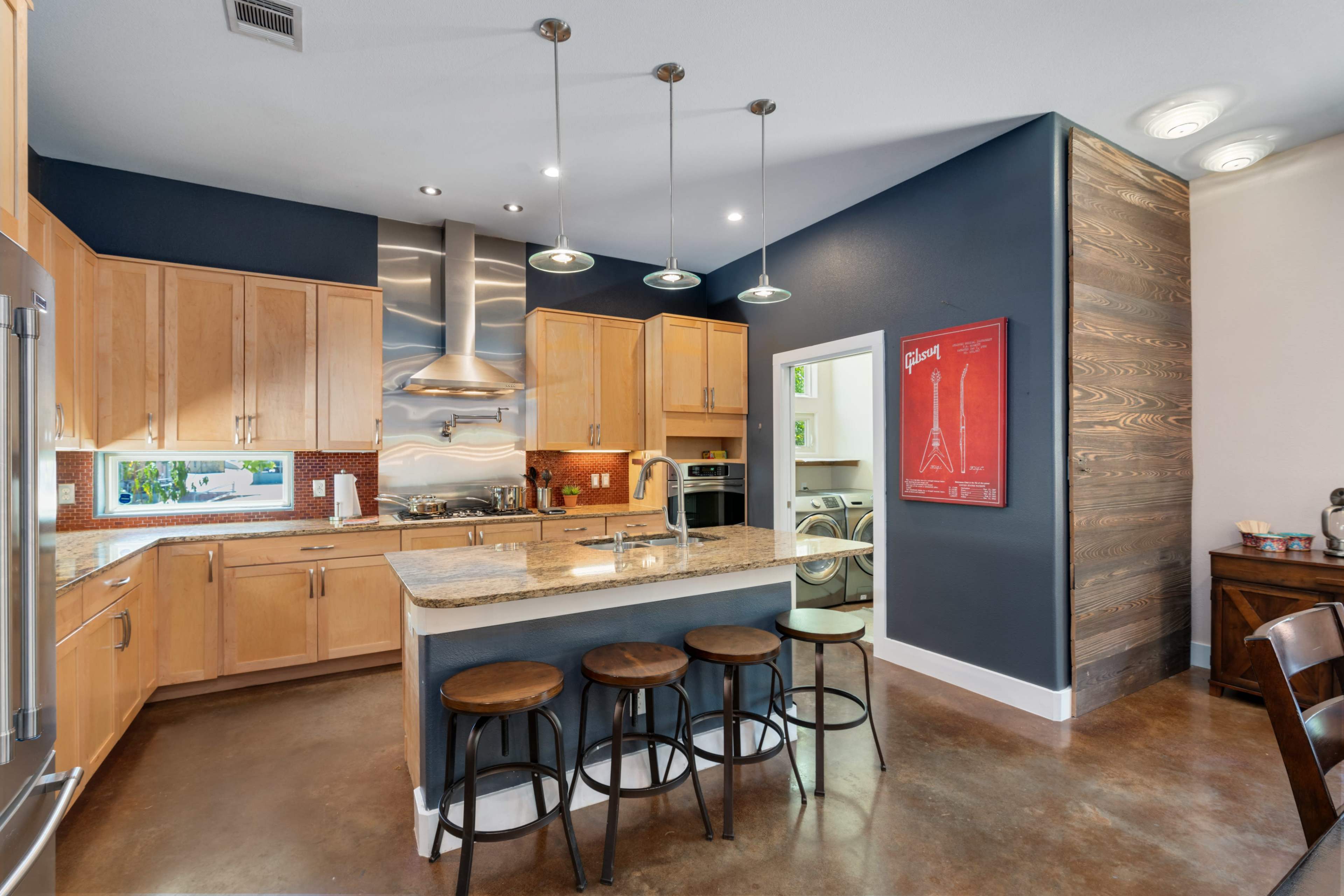 A modern kitchen features wooden cabinets, a granite countertop island with three stools, and stainless steel appliances.