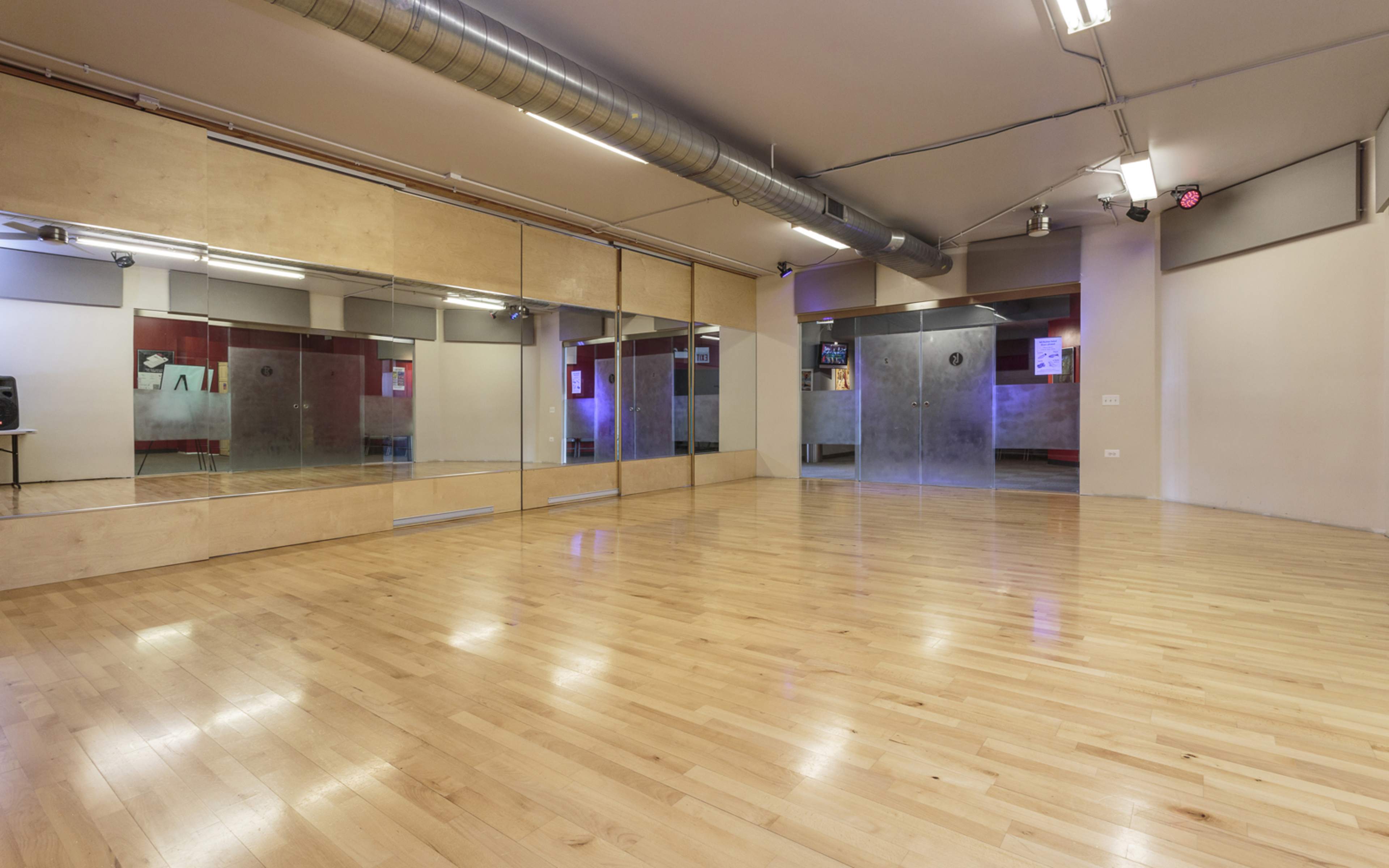 A dance studio features wooden flooring and large mirrors on one wall, with a minimalist design and dim lighting.
