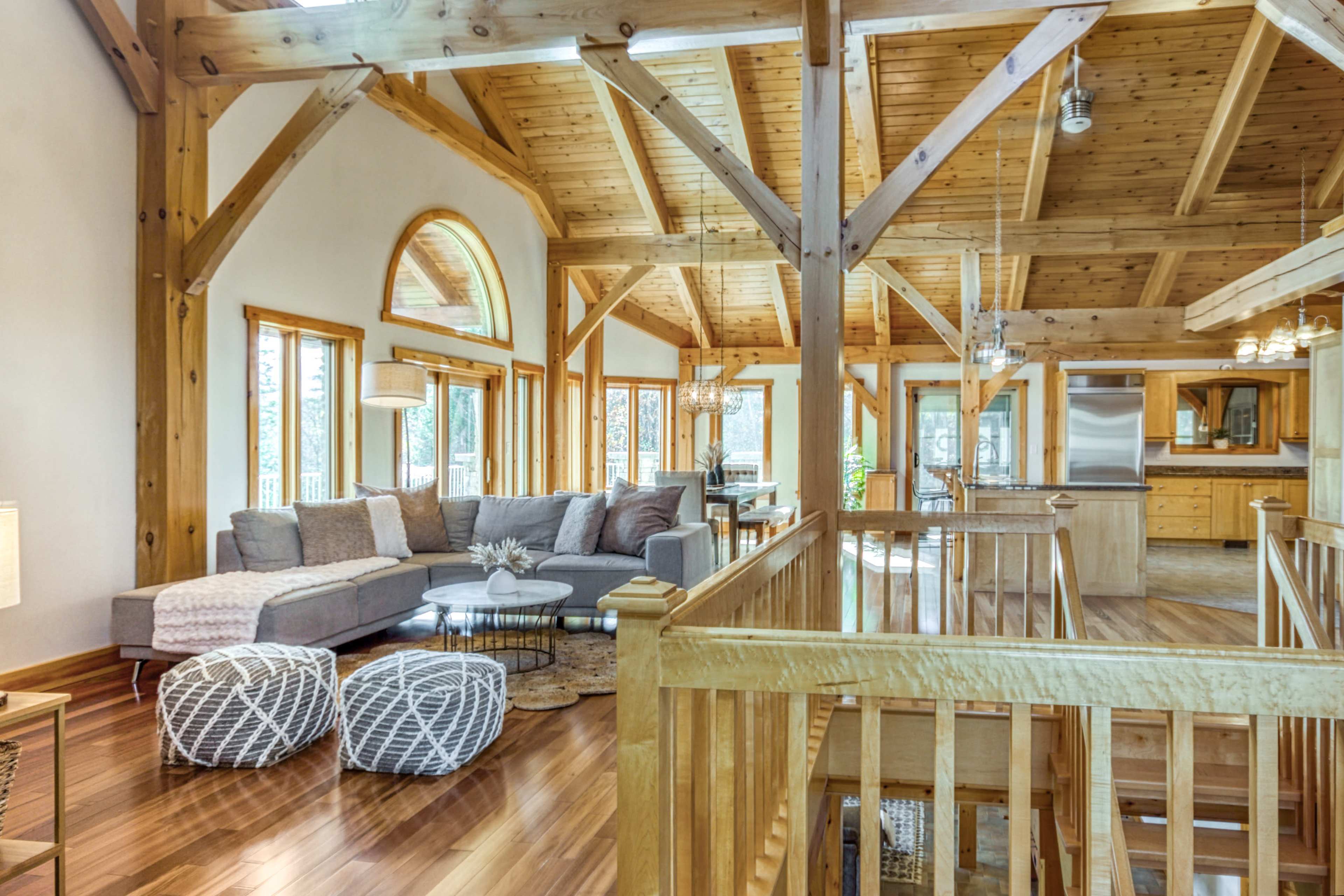 A spacious, open-plan living area with wooden beams, large windows, and a sectional sofa facing a light-colored kitchen.