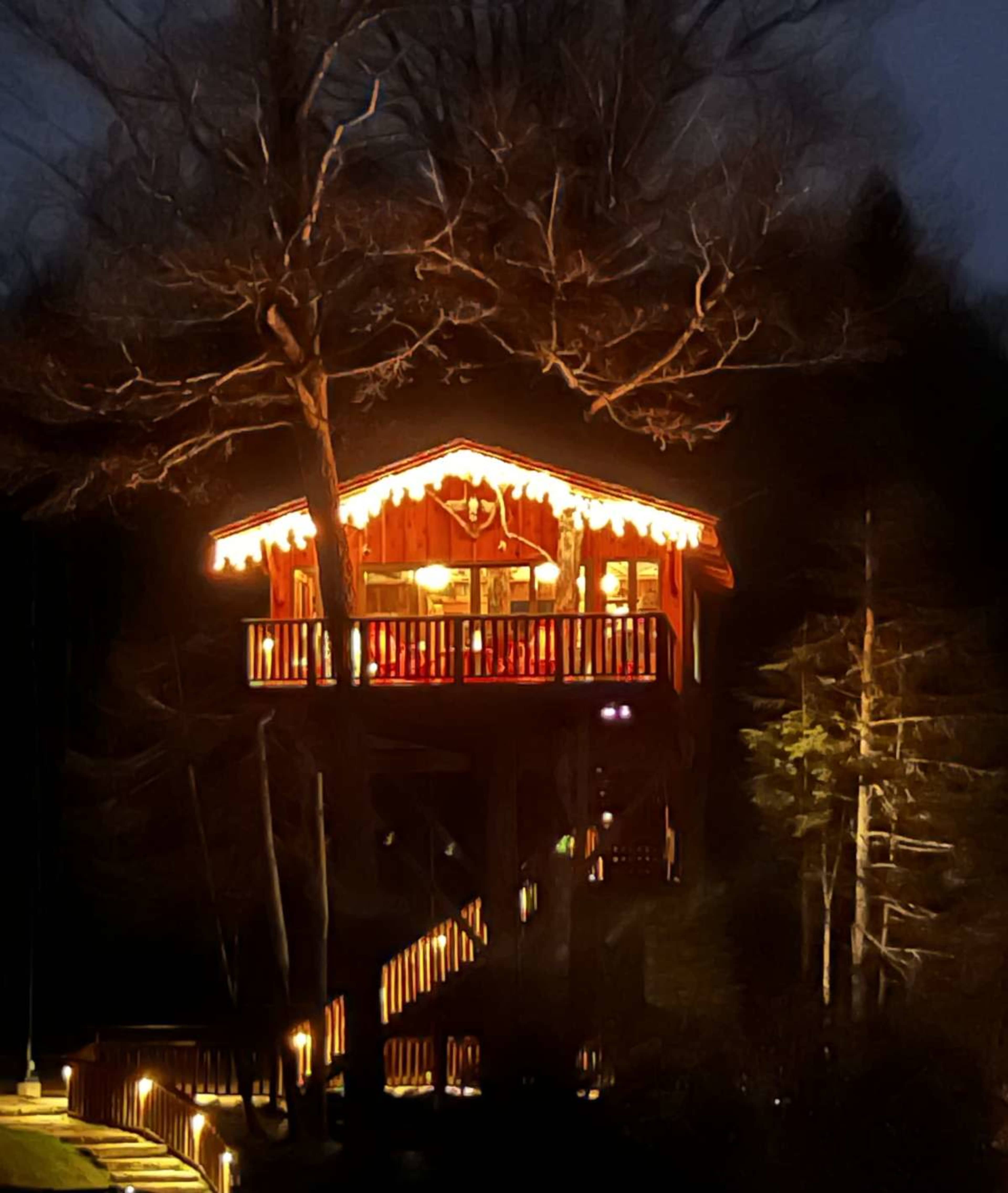 A brightly lit treehouse with festive decorations stands among dark trees at night.