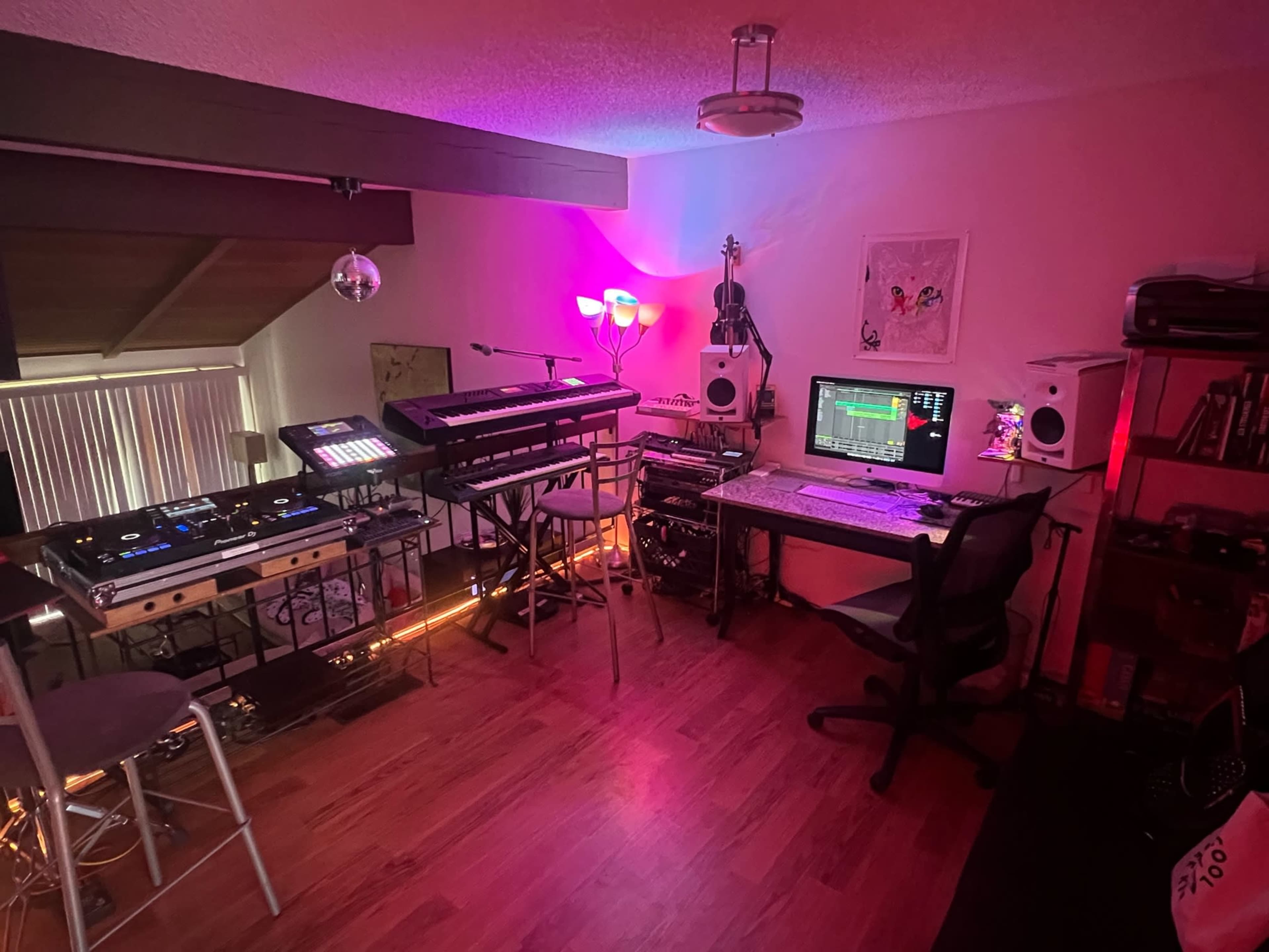 A music production studio with synthesizers, a computer setup, and various audio equipment arranged in a dimly lit room.