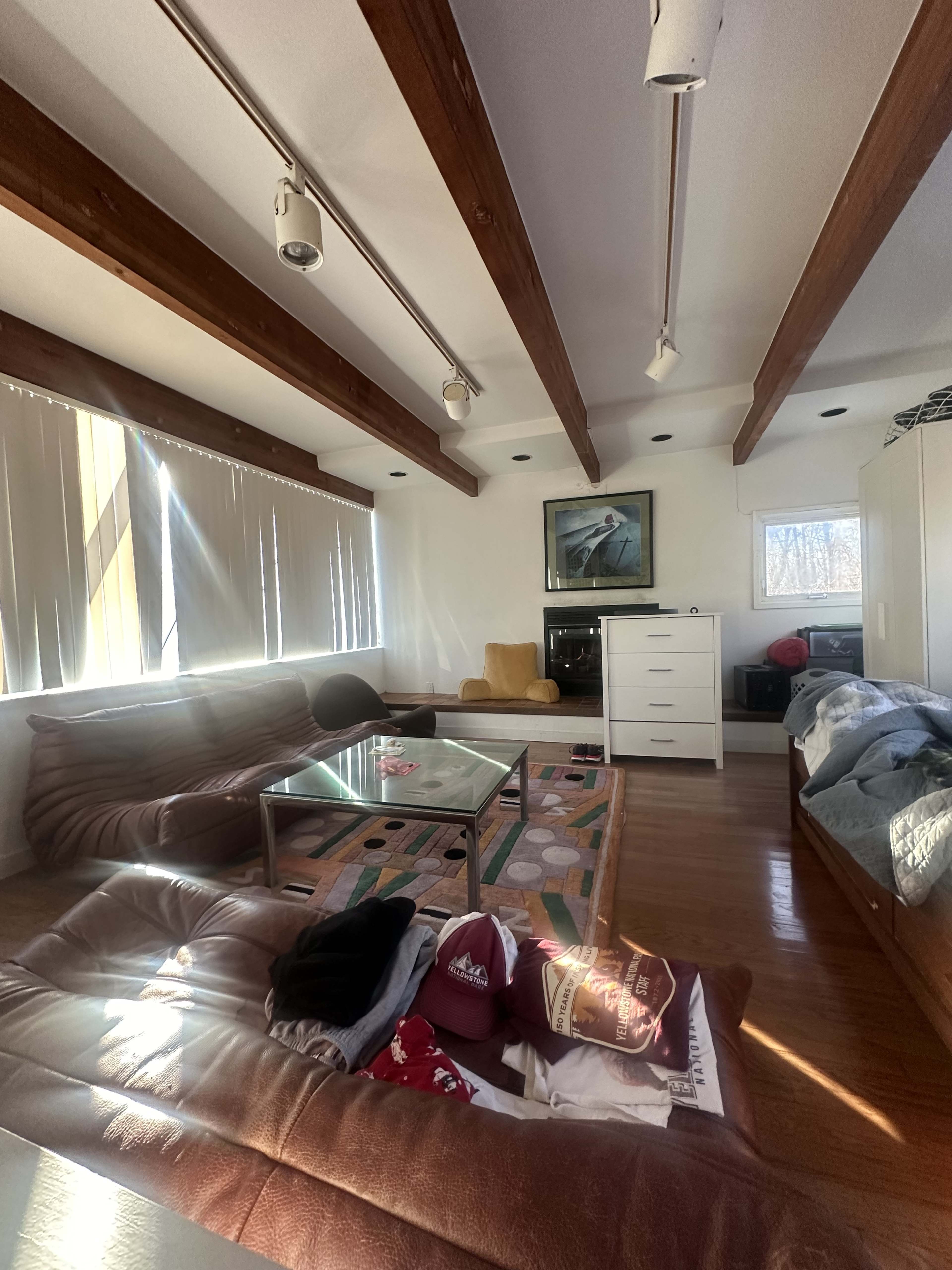 The image shows a spacious living room with wooden beam ceilings, featuring a coffee table, multiple seating areas, and a dresser against one wall.
