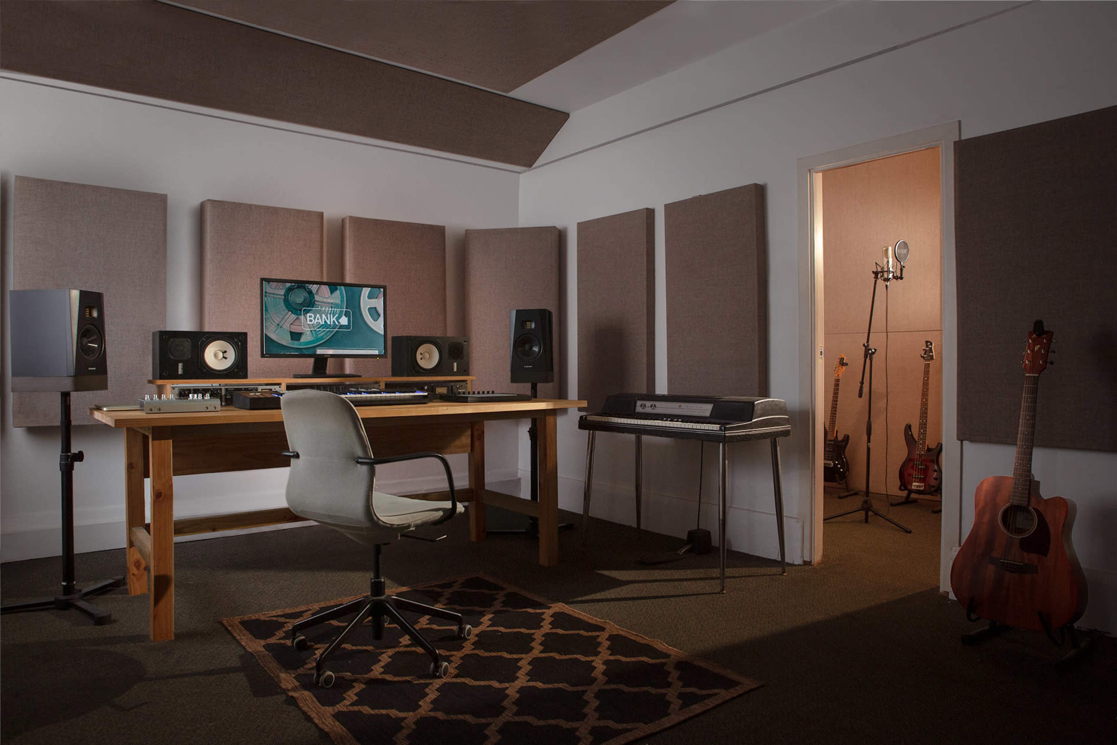 A music studio featuring a desk with audio equipment, speakers, a microphone setup in a corner, and various musical instruments on display.