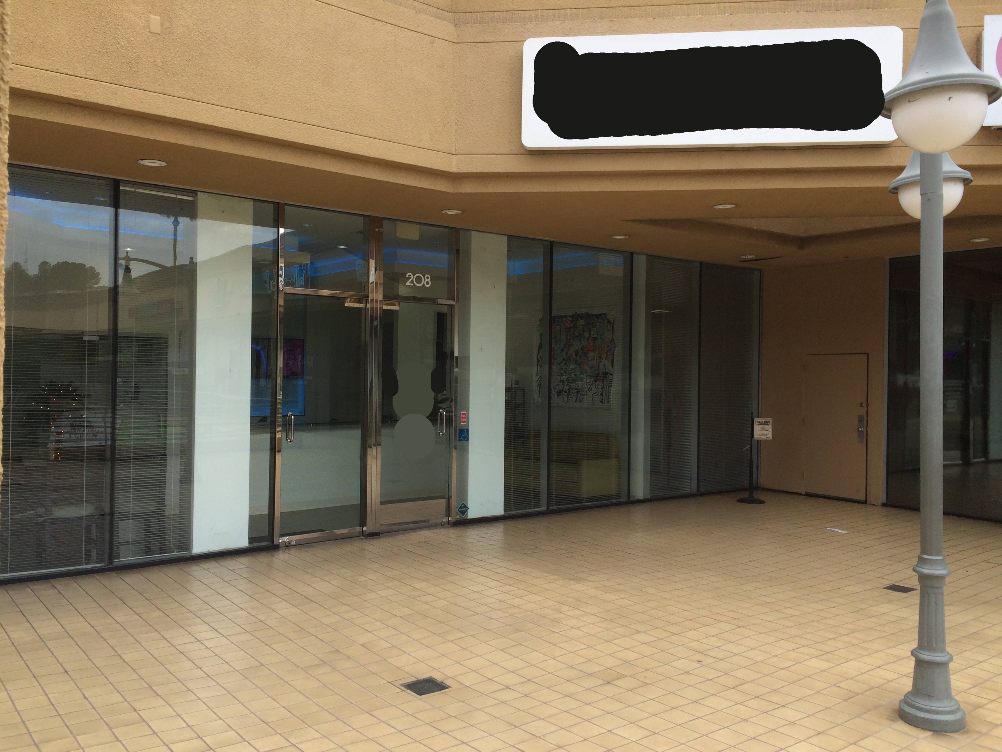 The image shows the entrance of a storefront with large glass windows and a tiled walkway in front.