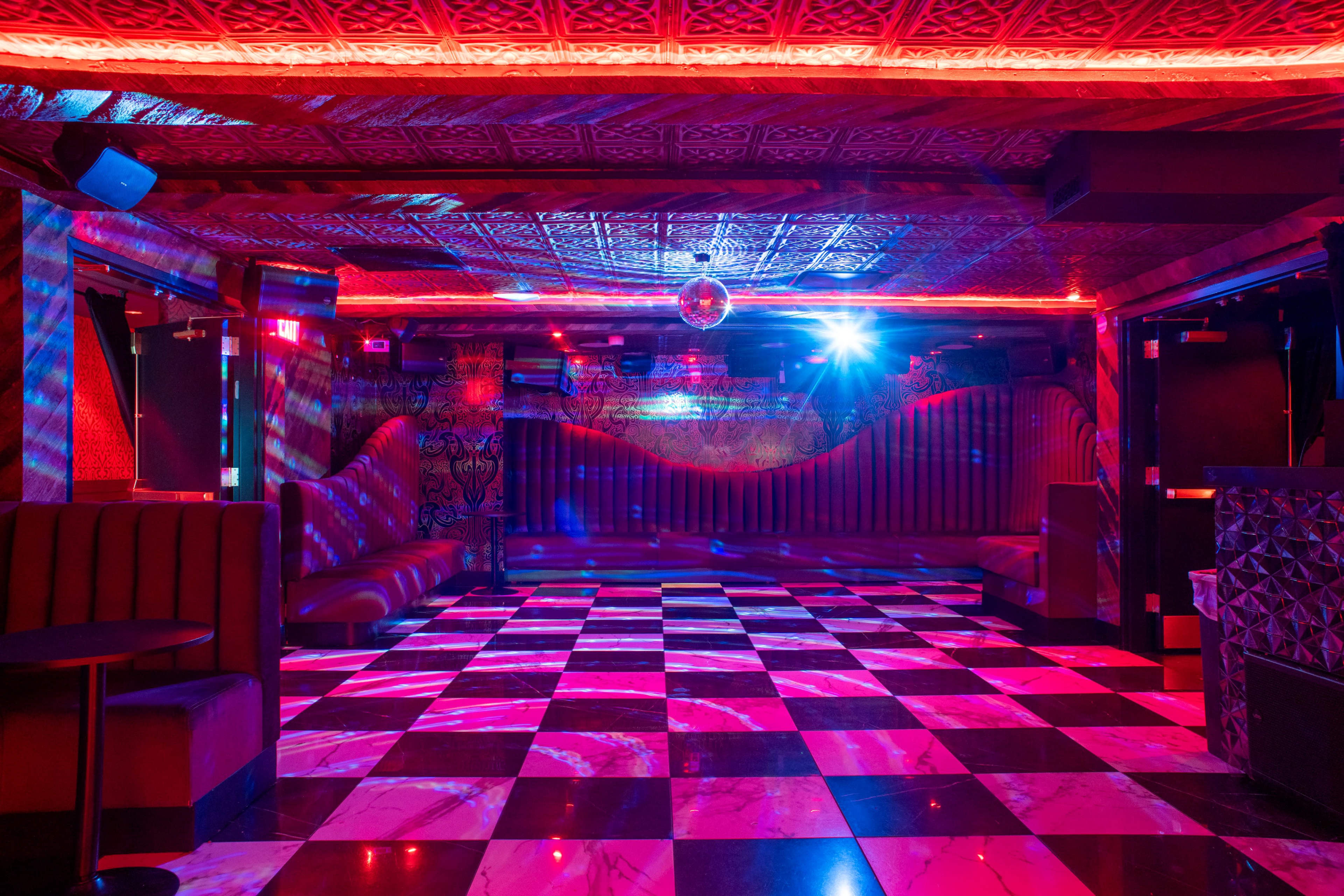 The image shows a dimly lit nightclub with a checkered floor, colorful lighting patterns, and a mirrored disco ball.