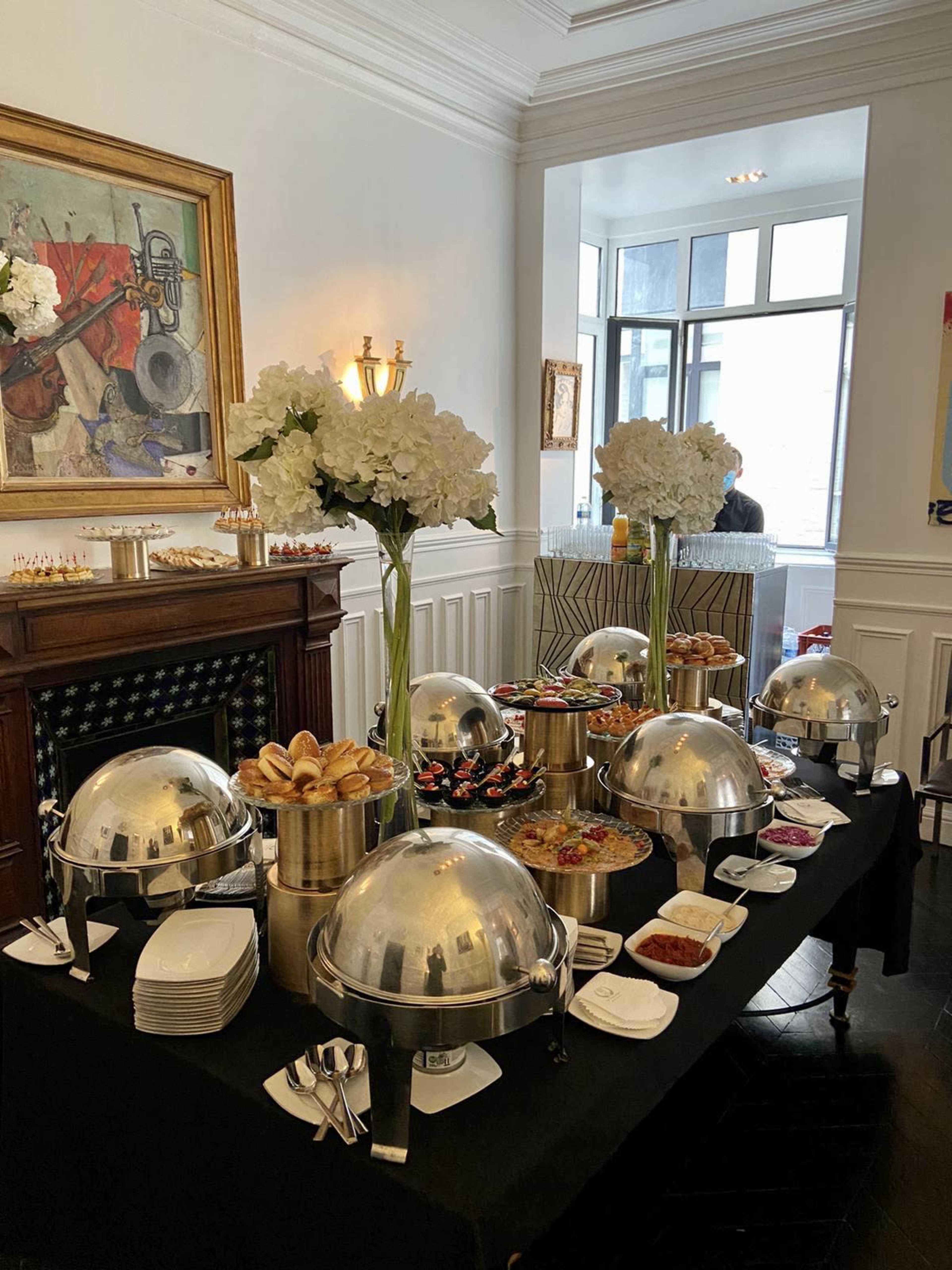 The image shows a buffet setup with silver chafing dishes and an arrangement of flowers in a well-decorated room.