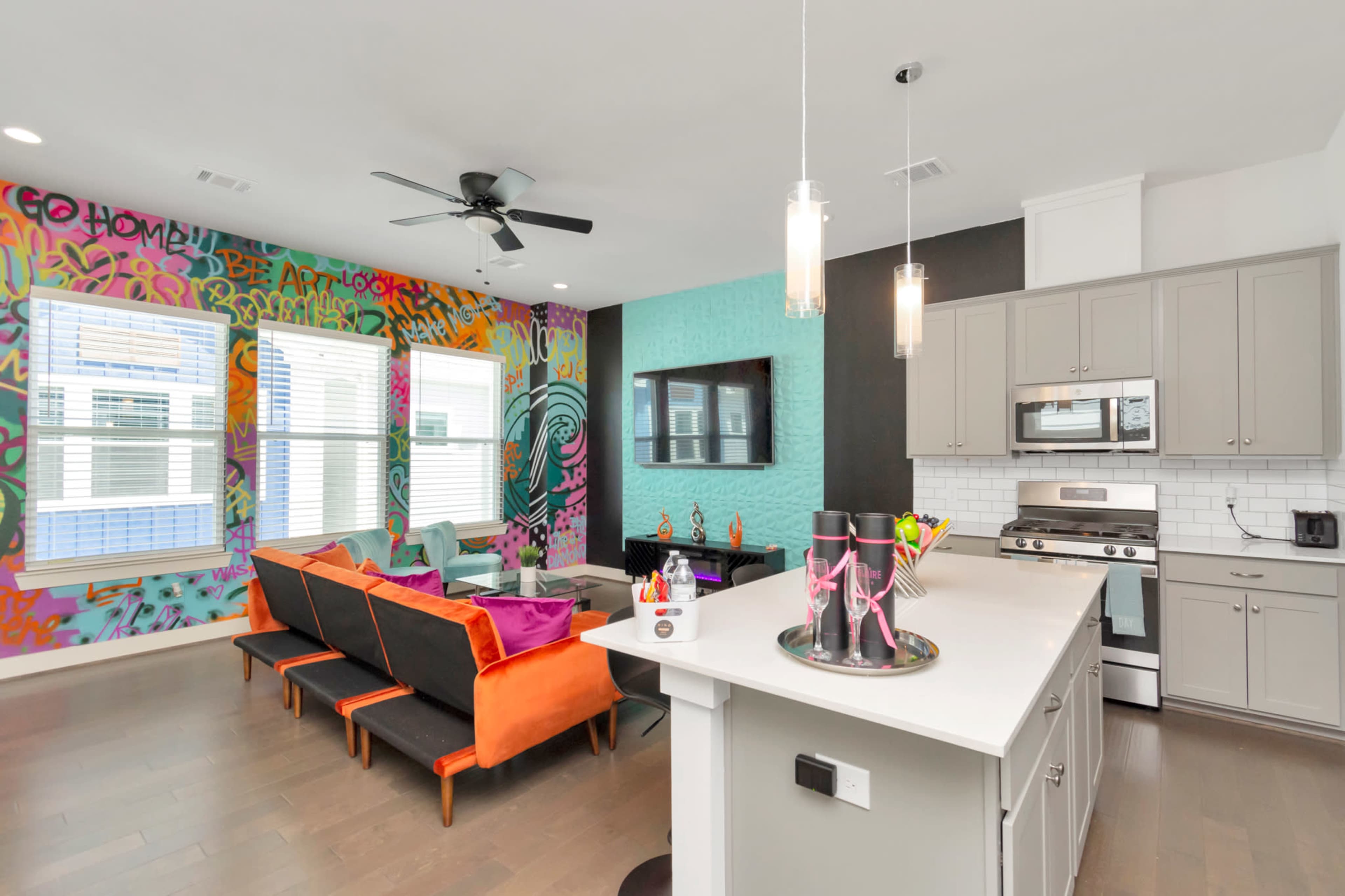 A modern living space with colorful graffiti walls, a sectional sofa, and a kitchen island featuring pendant lights.
