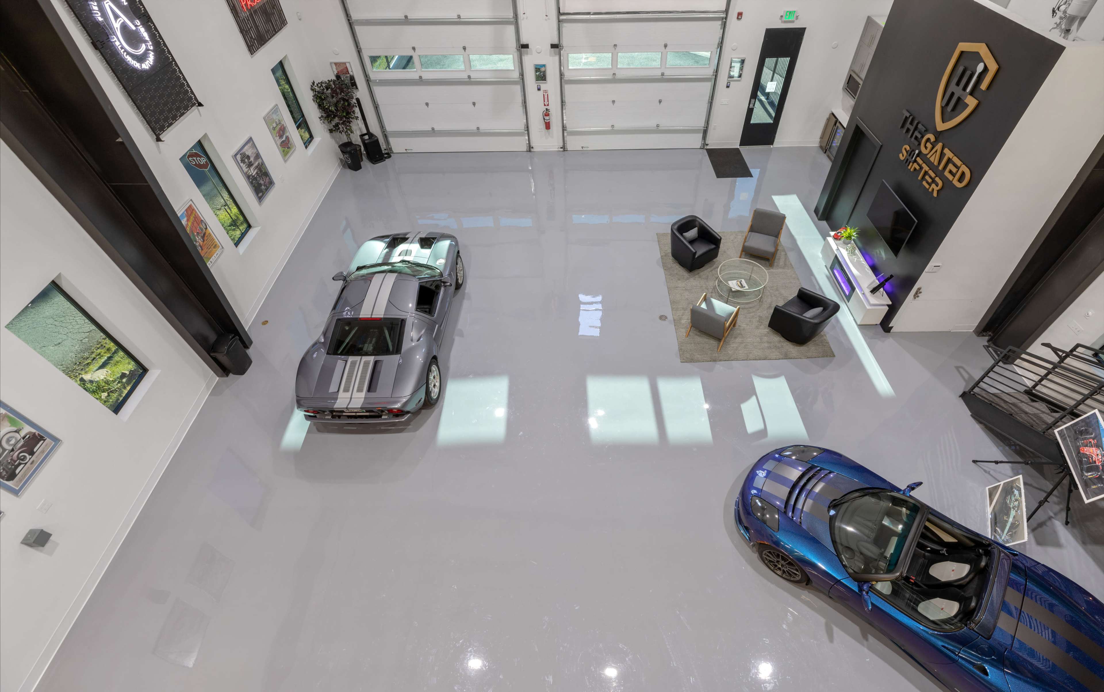 The image shows an upscale garage featuring two luxury cars, sleek concrete flooring, and modern furnishings.