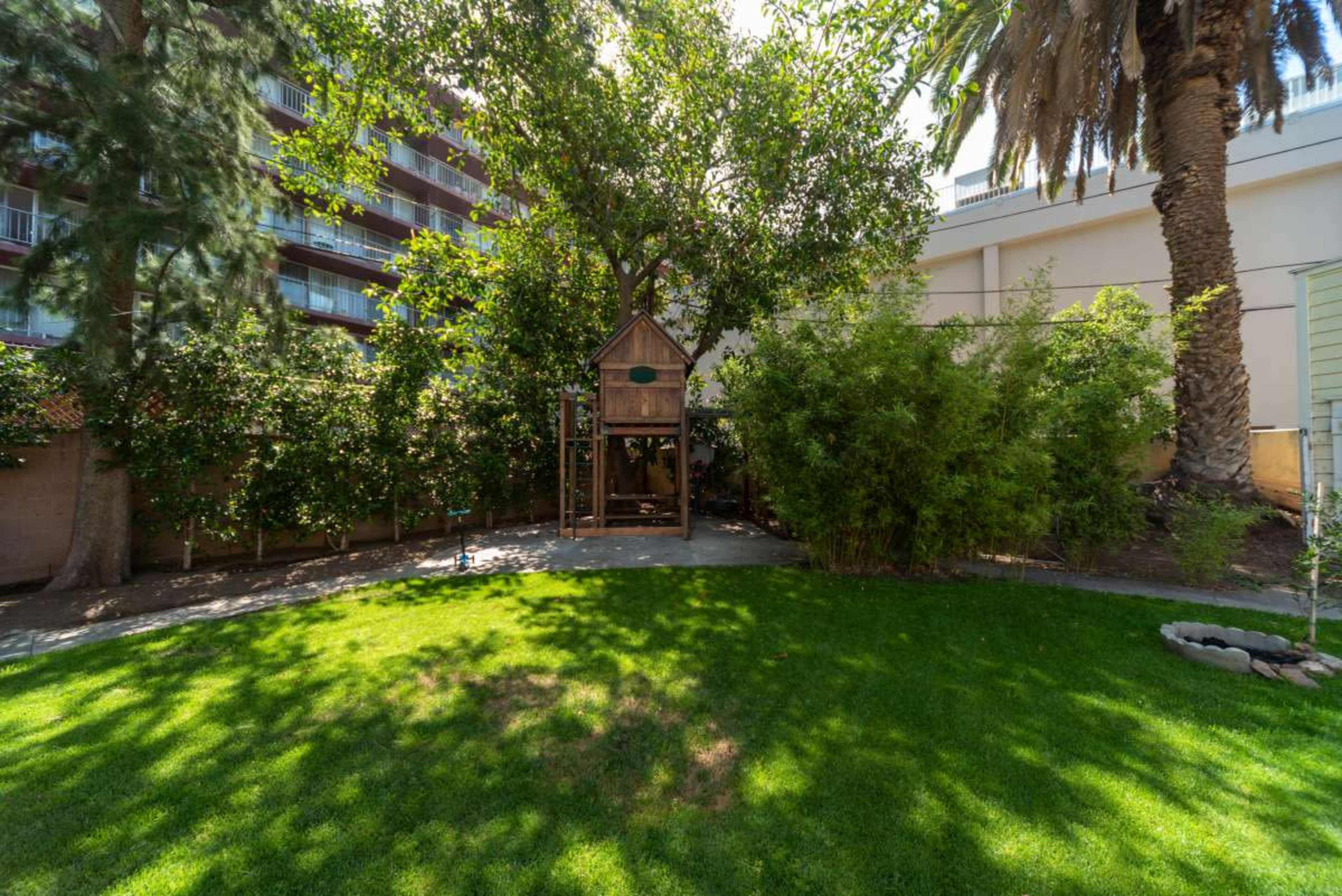 A lush green backyard featuring a wooden treehouse surrounded by trees and shrubs.
