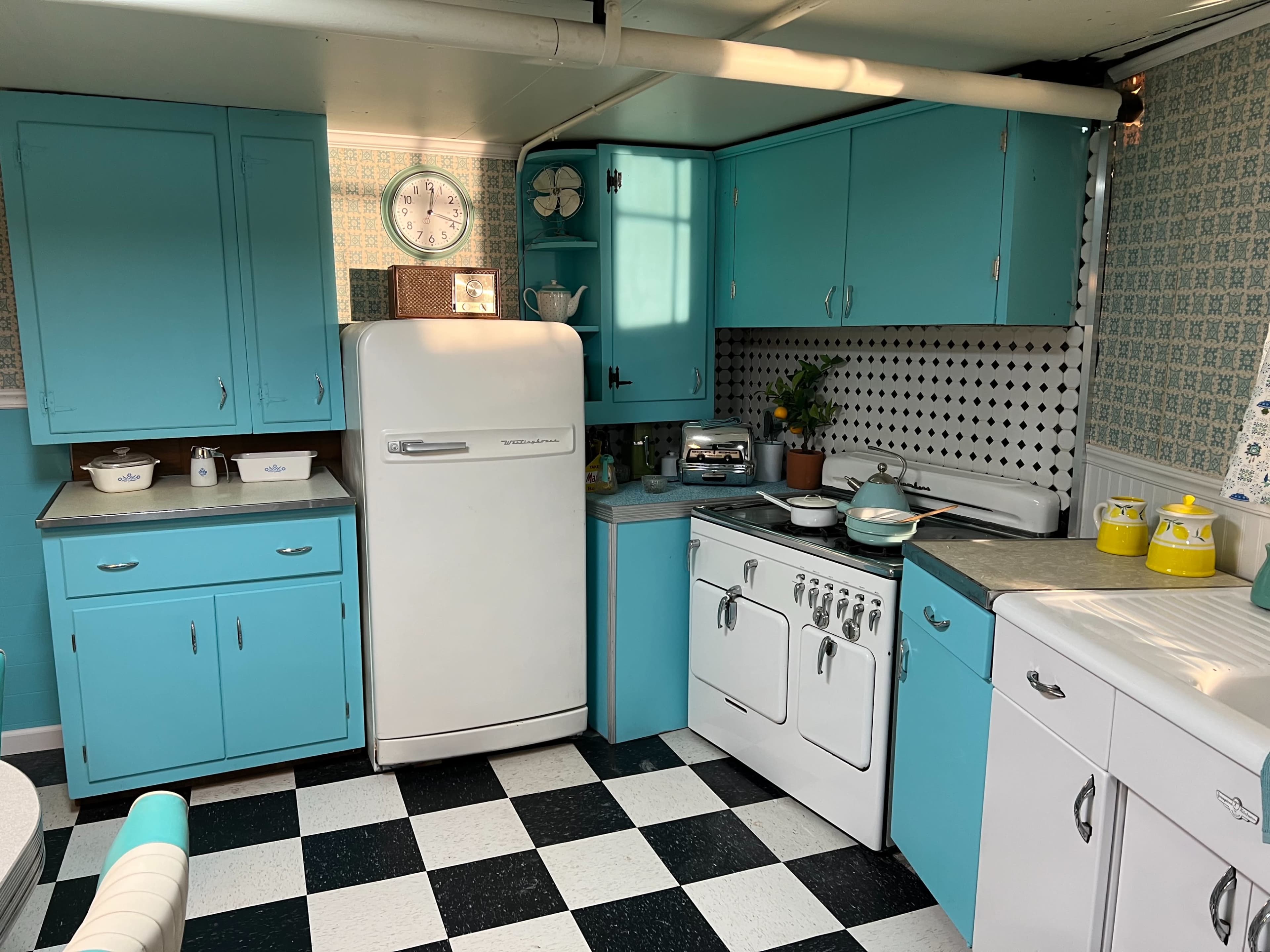A vintage kitchen with turquoise cabinets, a white refrigerator, and black and white checkered flooring.
