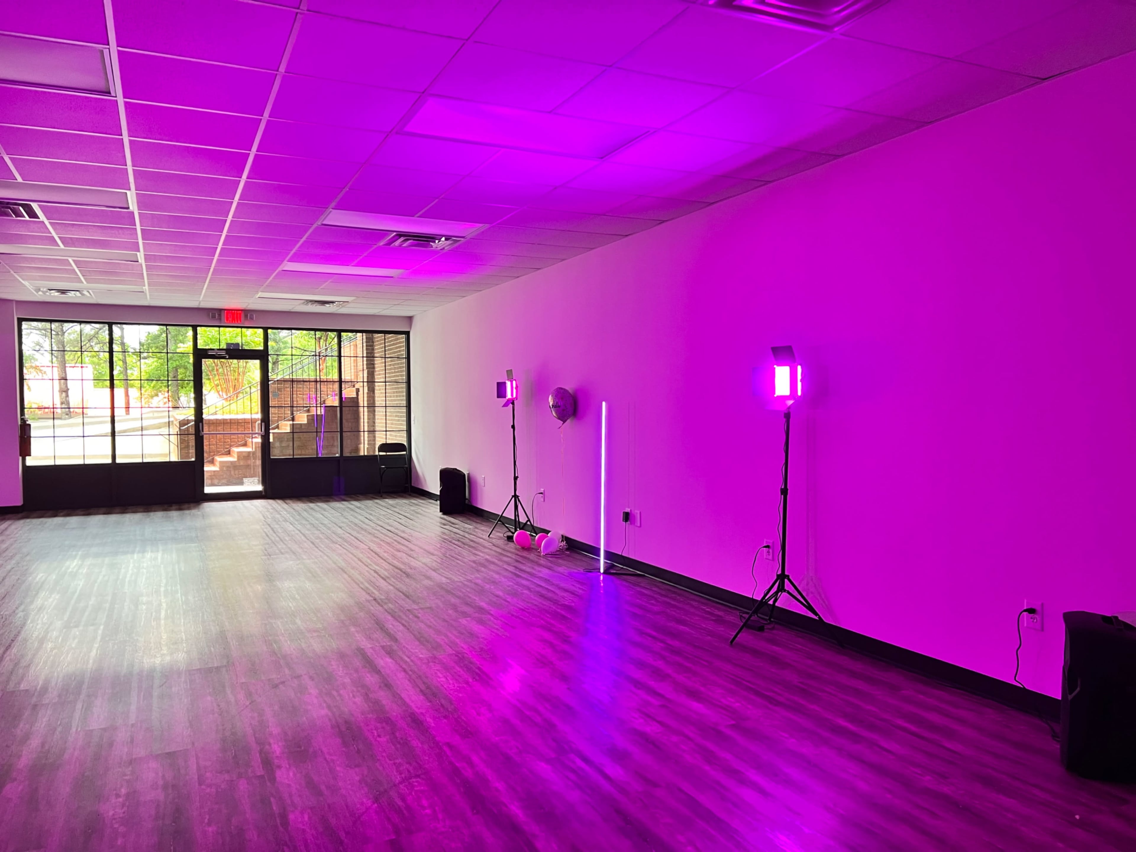 A spacious, empty room with purple lighting, two floor lamps, and large windows along one wall.
