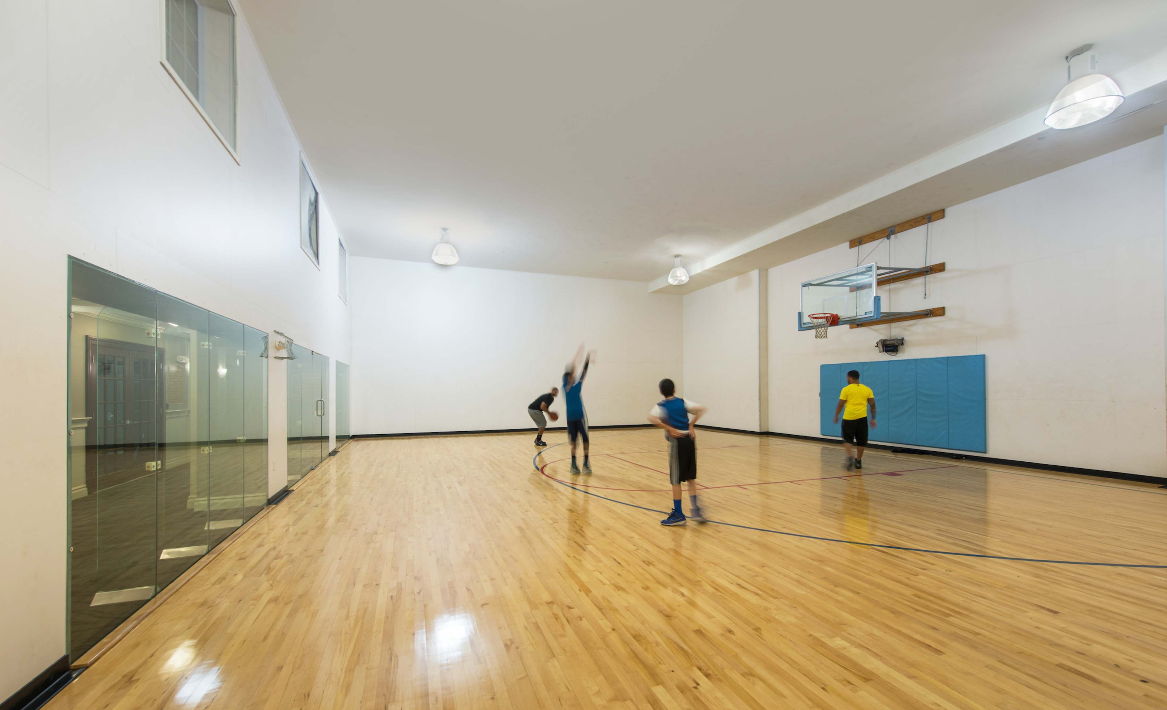 Three players are practicing basketball in a well-lit gym with wooden flooring and a hoop at one end.