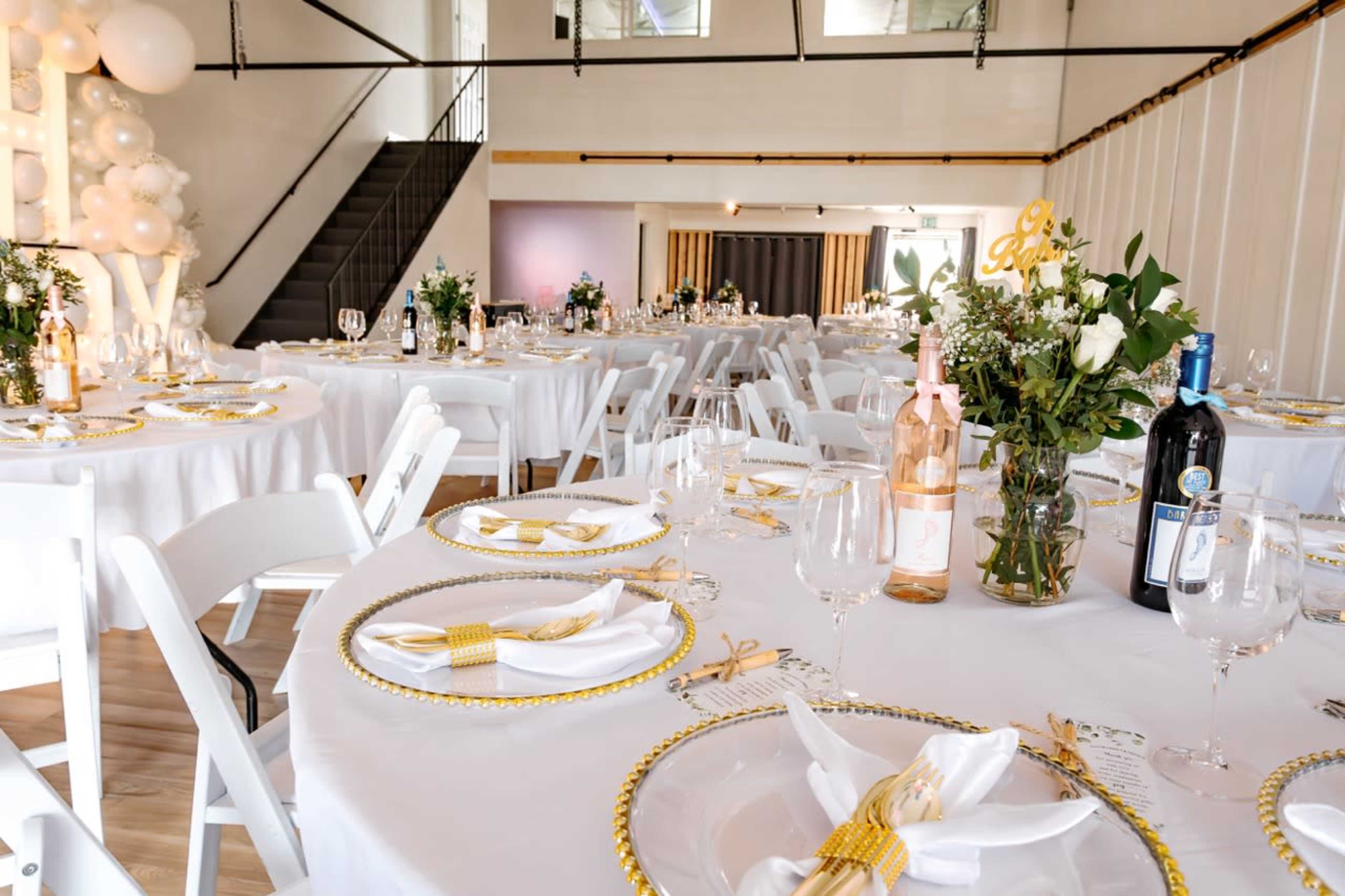 A beautifully arranged event space with round tables set with white tablecloths, golden accents, and floral centerpieces.