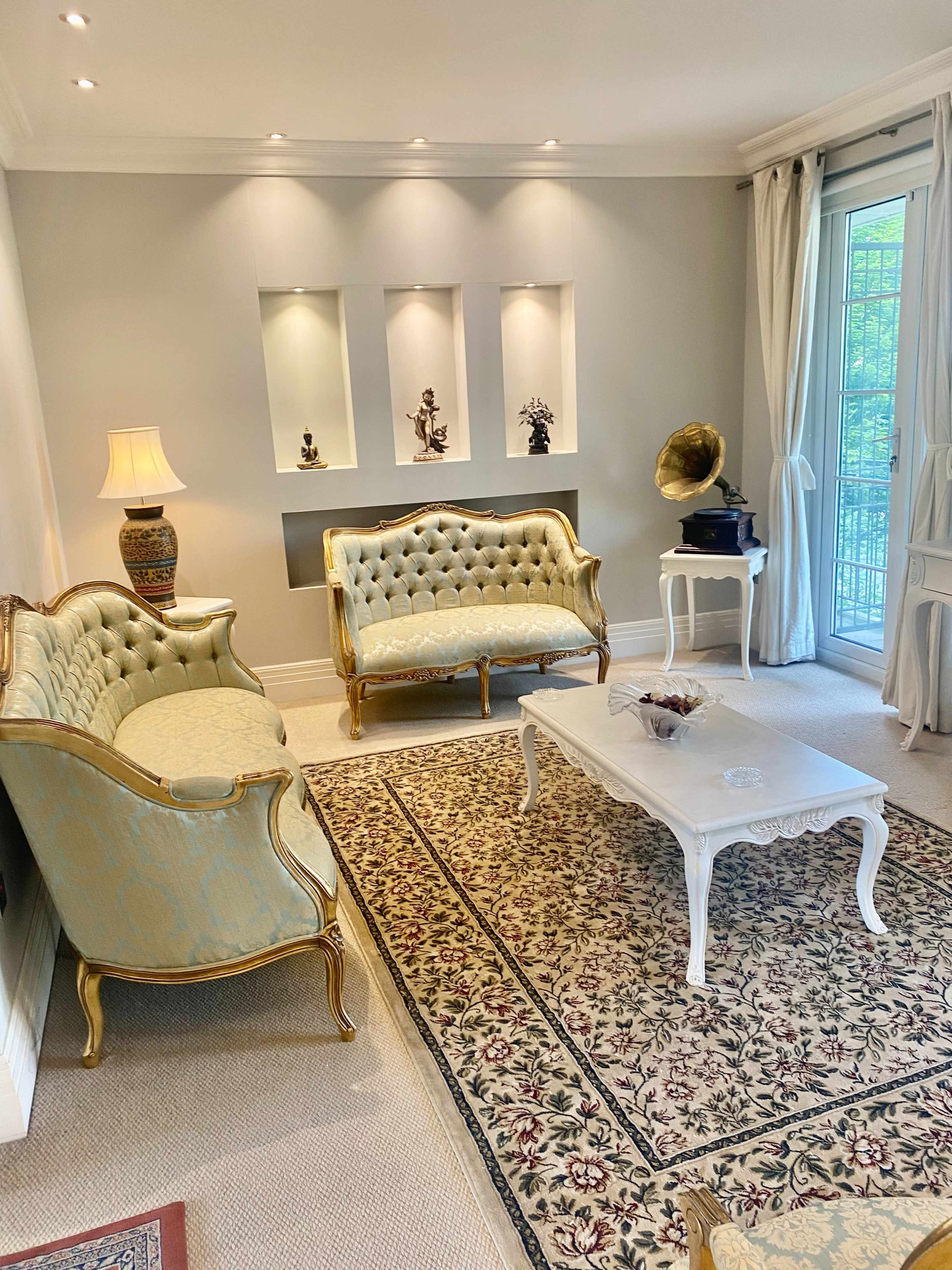 A light-colored living room with two ornate sofas, a decorative coffee table, and a patterned area rug.