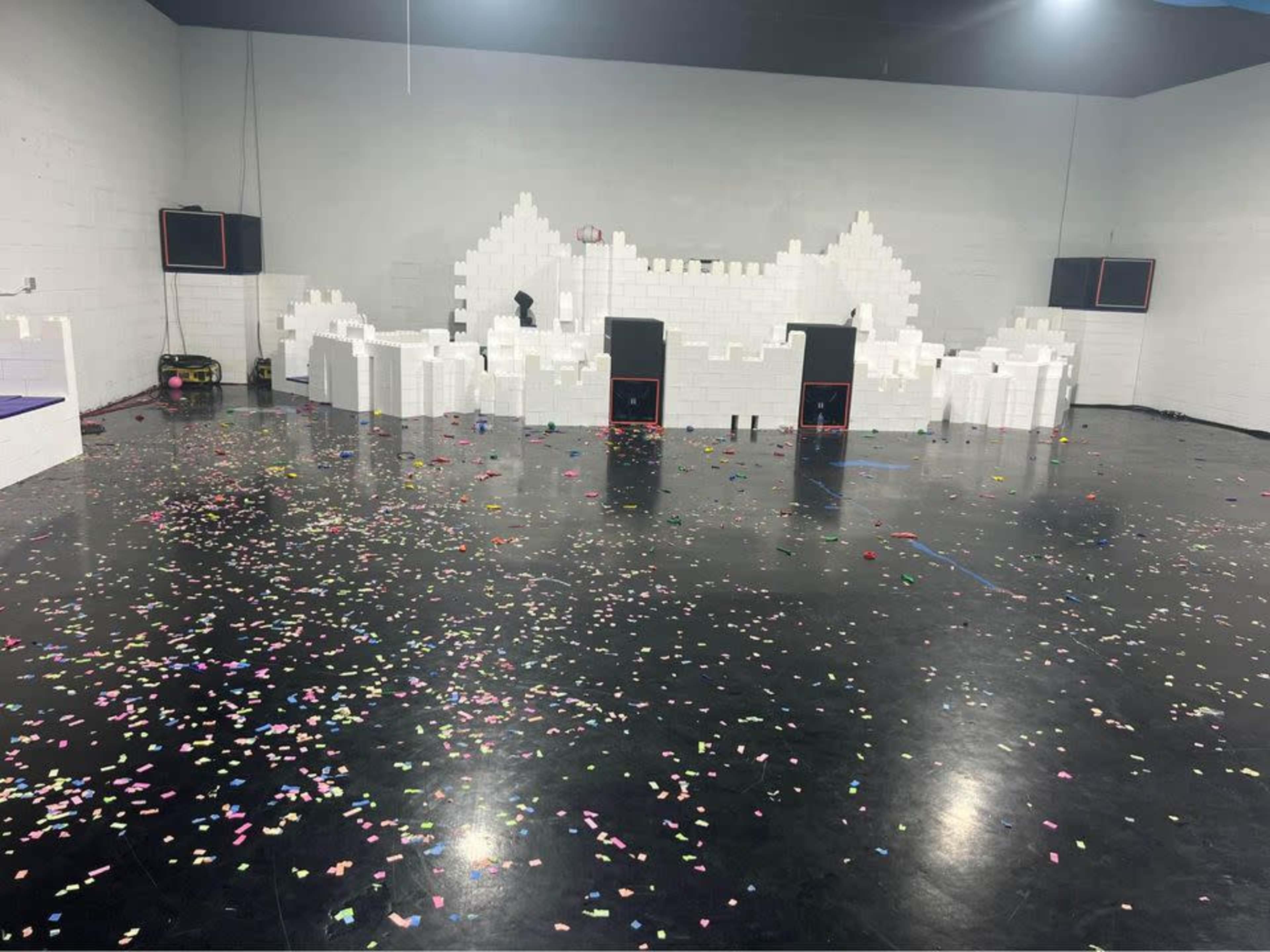 The image shows a large room with scattered colorful confetti on the black floor and a structure made of white foam blocks in the background.