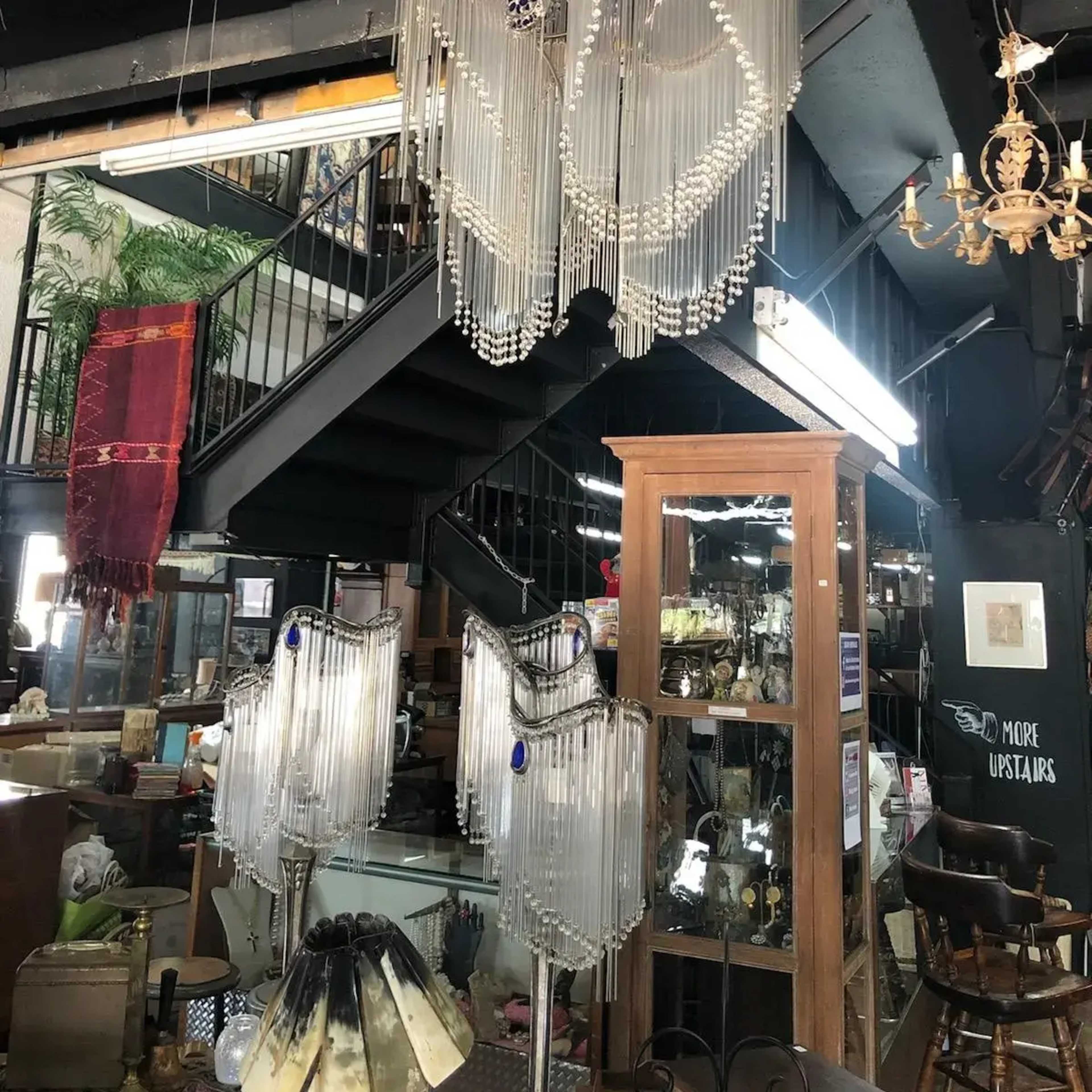 The image shows a vintage store interior featuring multiple chandeliers, glass display cases, and a staircase in the background.