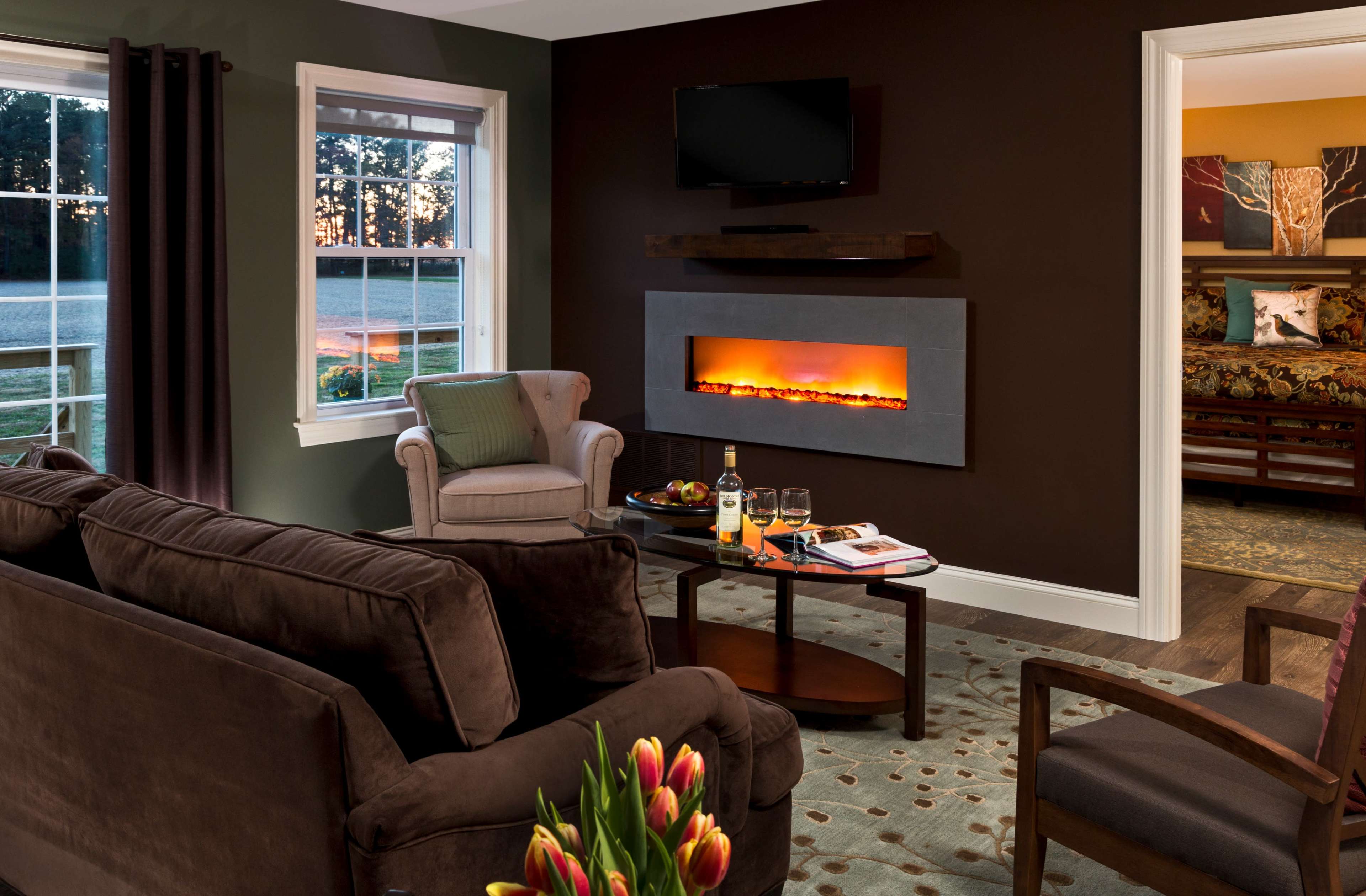 The living room features a modern electric fireplace, comfortable seating, and large windows overlooking a landscaped outdoor area.