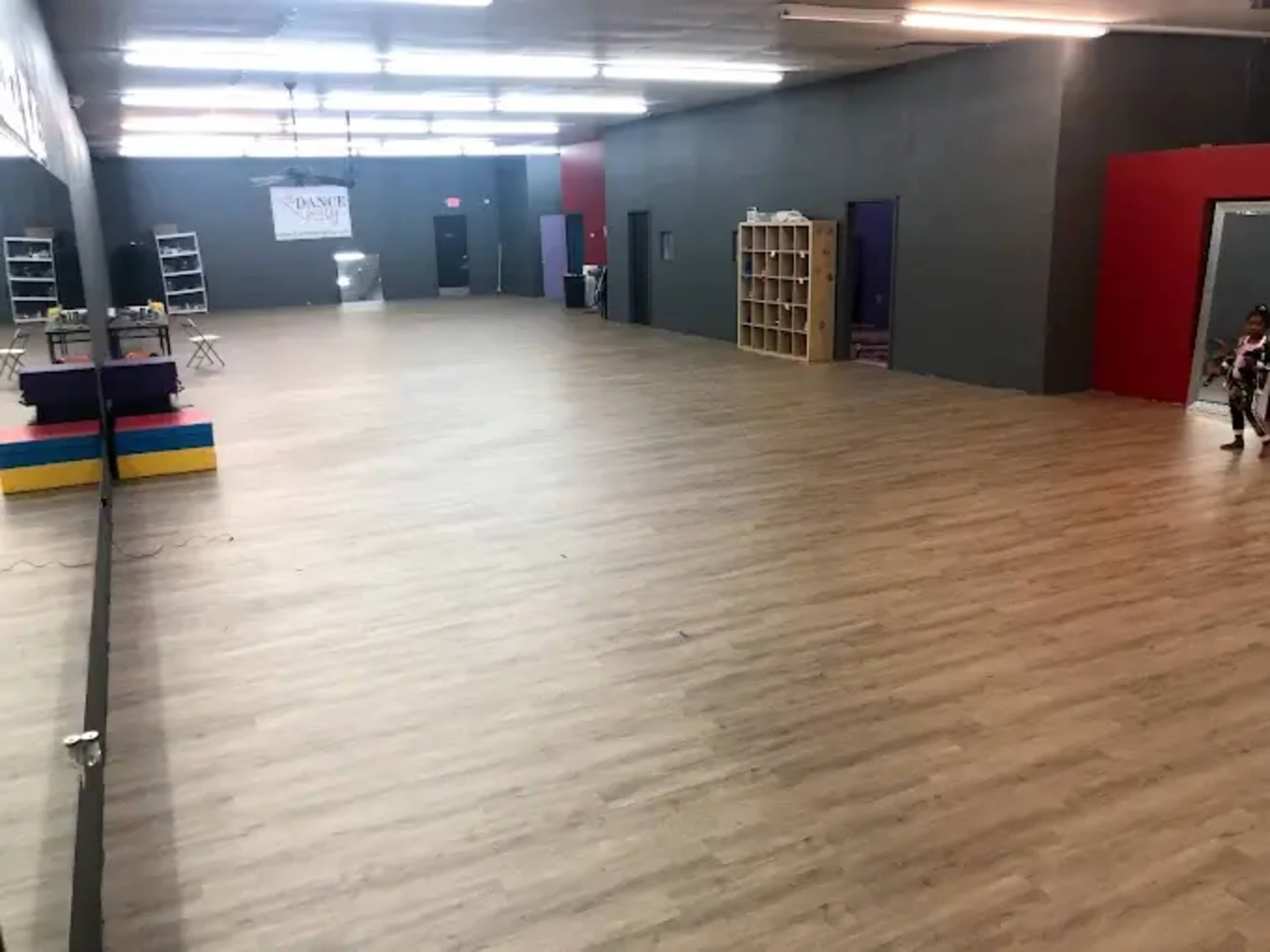 The image shows a spacious, empty indoor area with wooden flooring and colorful blocks arranged near one wall.
