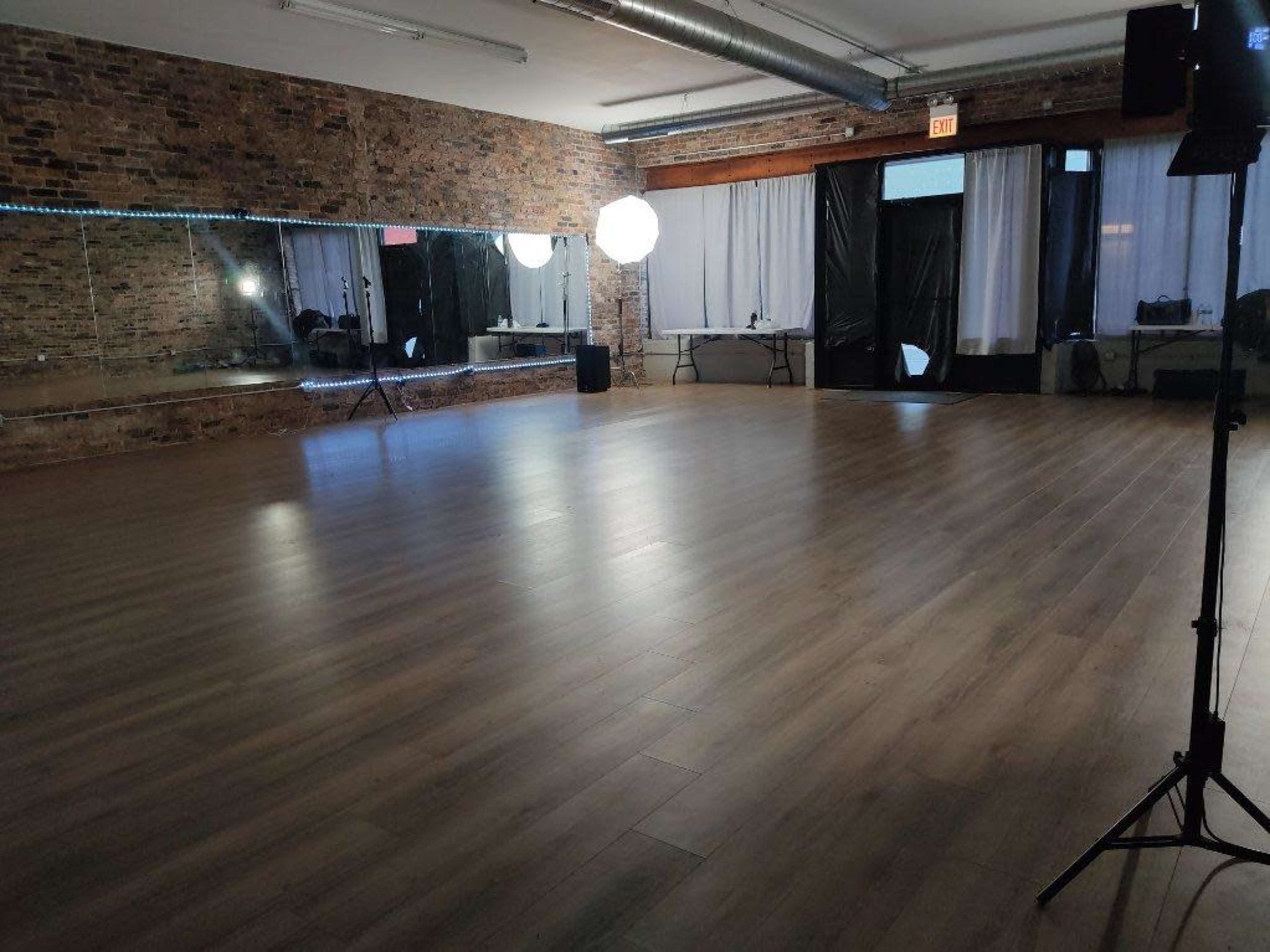 A spacious studio features wooden flooring, large mirrors, and soft lighting fixtures.