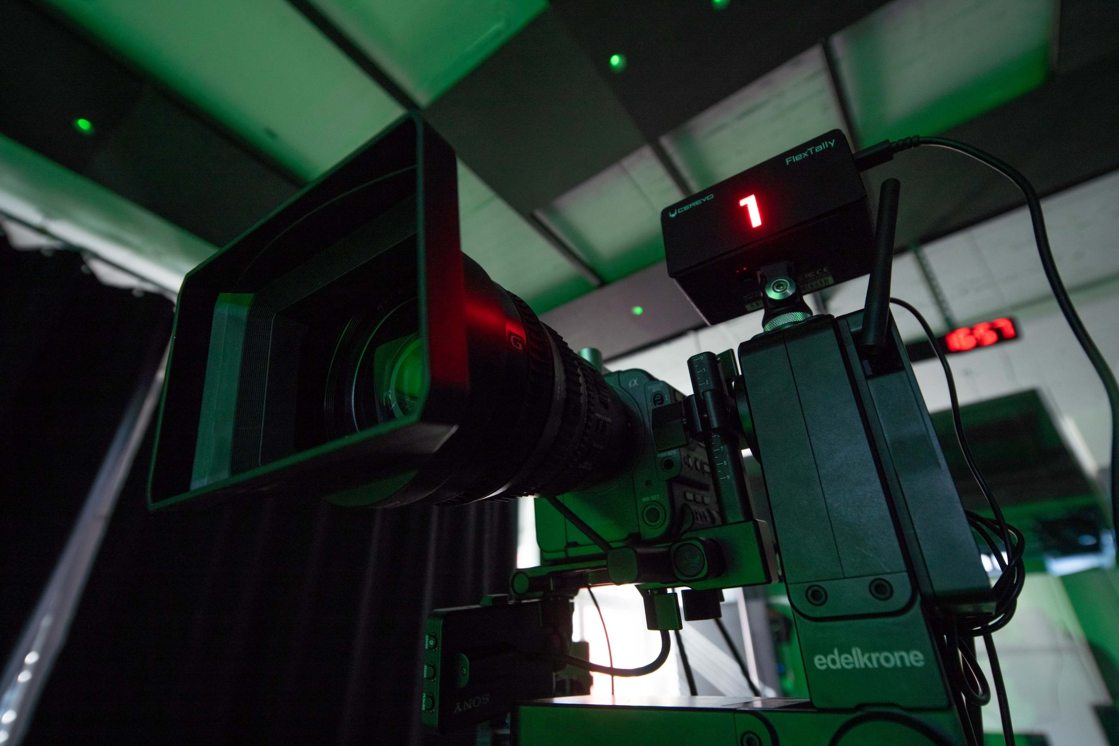 A camera mounted on a tripod, equipped with a large lens, displays a digital number "1" on an attached monitor.