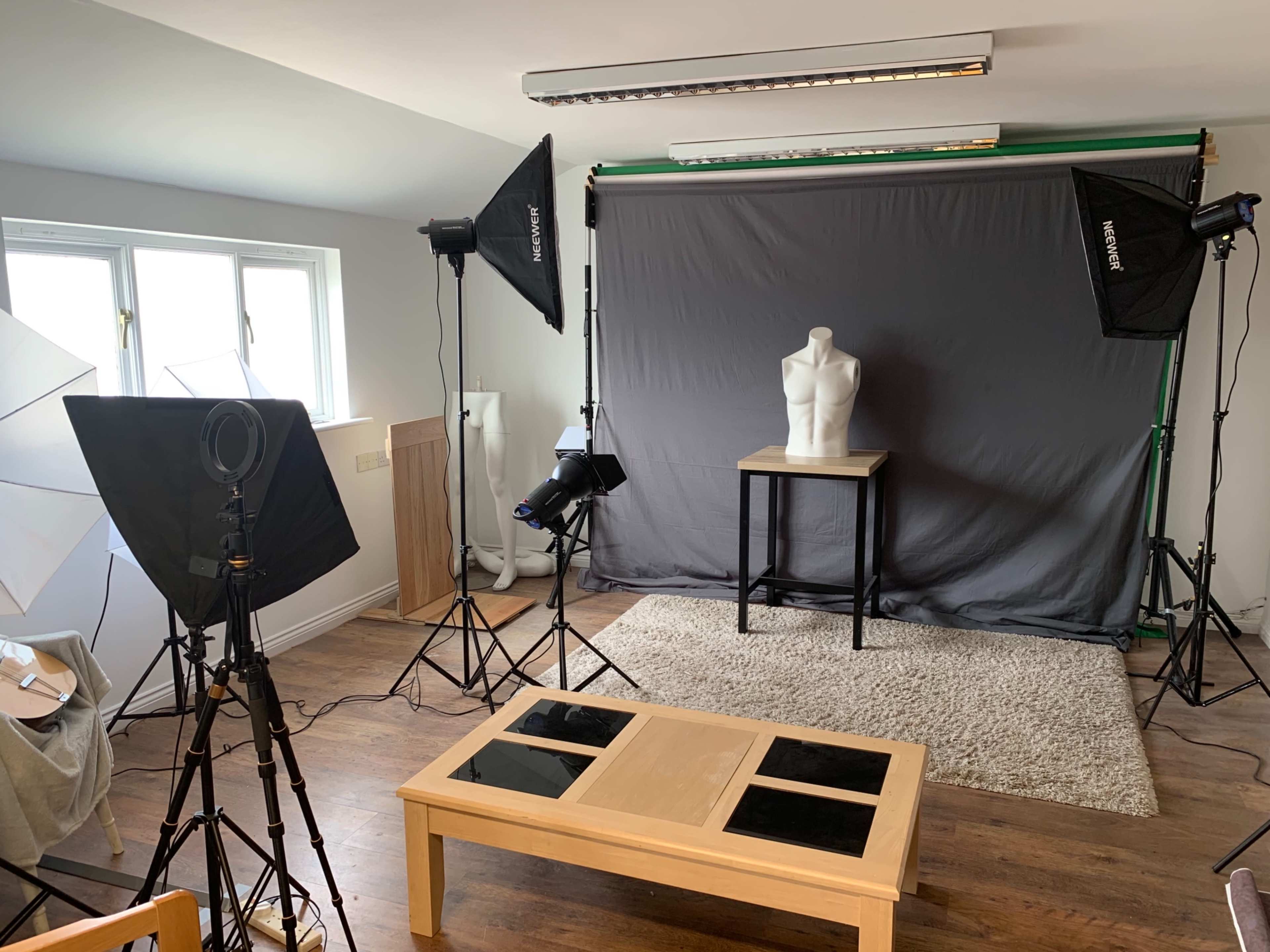 The image shows a photography studio with a dress form on a table, surrounded by lighting equipment and backdrops.