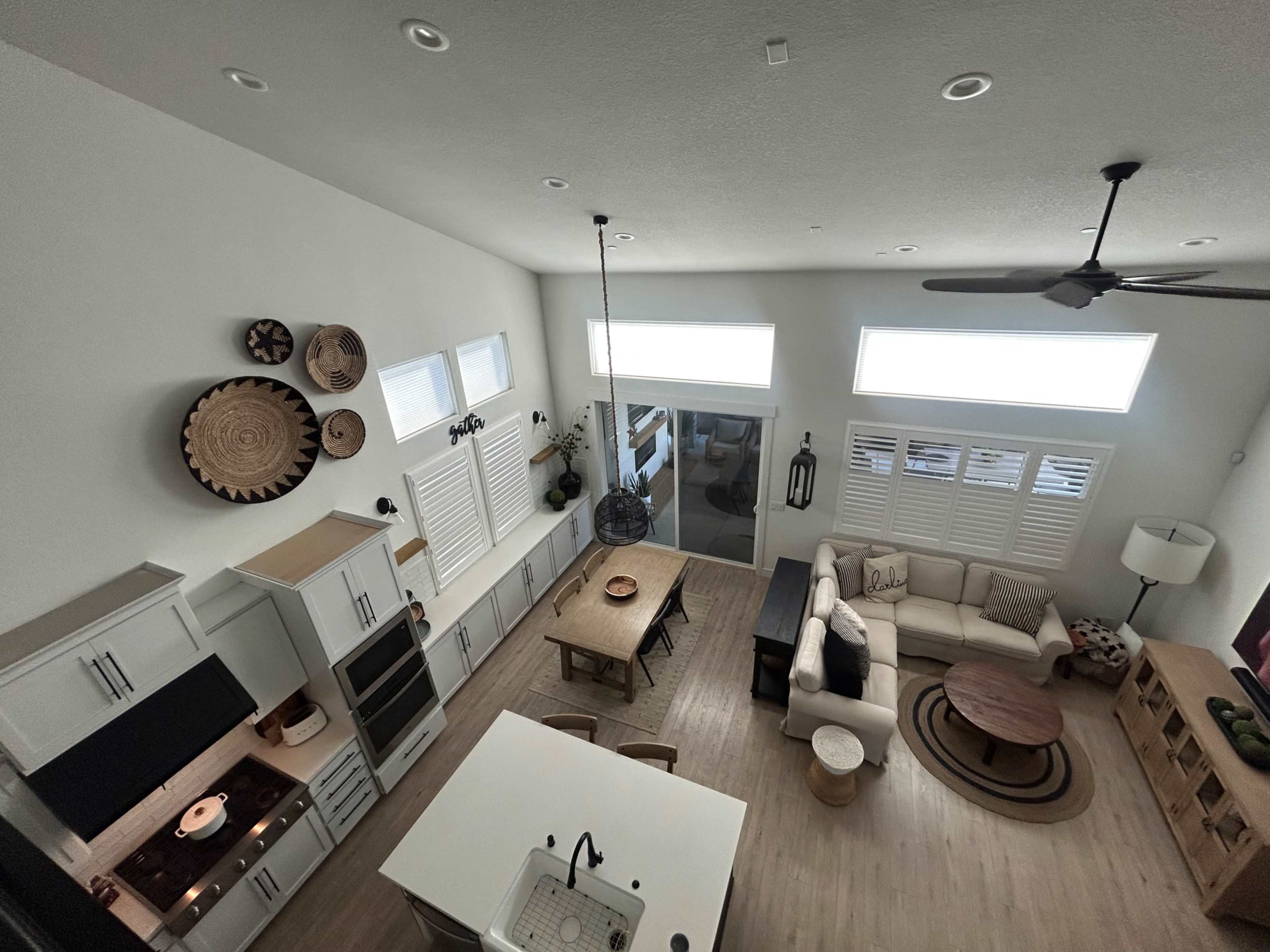 The image shows an overhead view of a modern, open-concept living and dining area with large windows, a kitchen island, a dining table, and a seating area with a couch and coffee table.