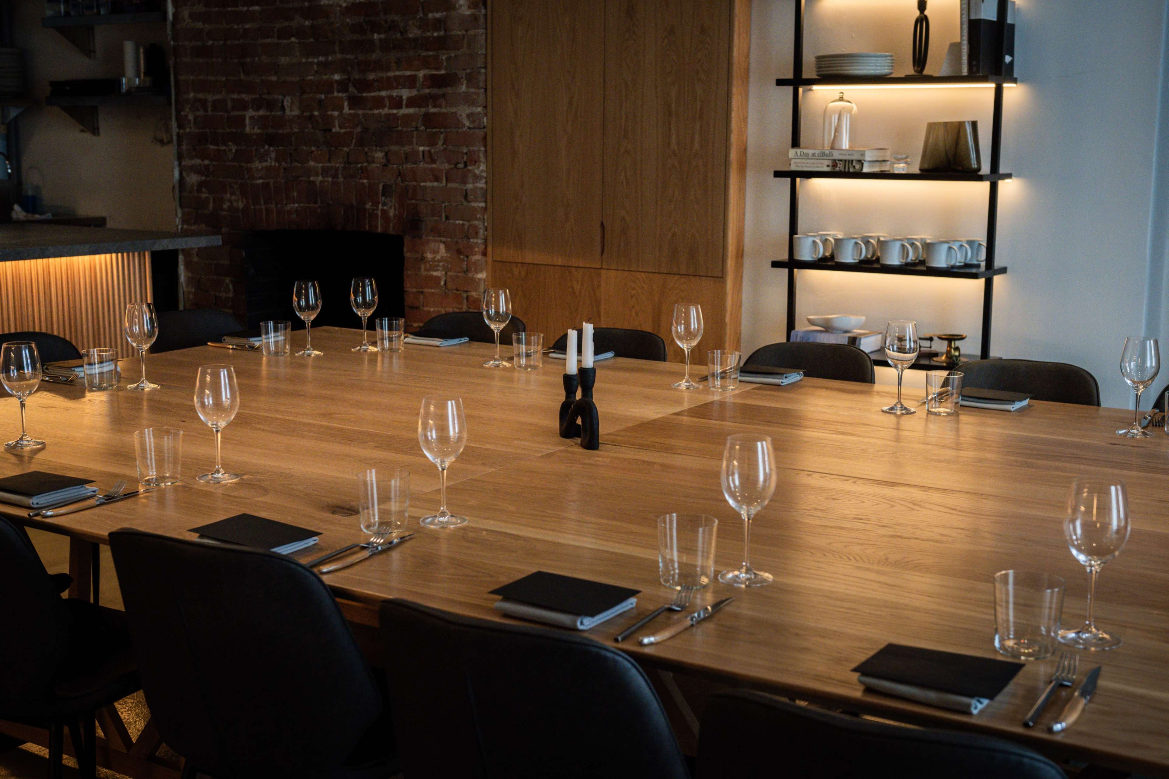 A long wooden dining table is set for a formal meal, with wine glasses, menus, and plates arranged neatly at each place setting.