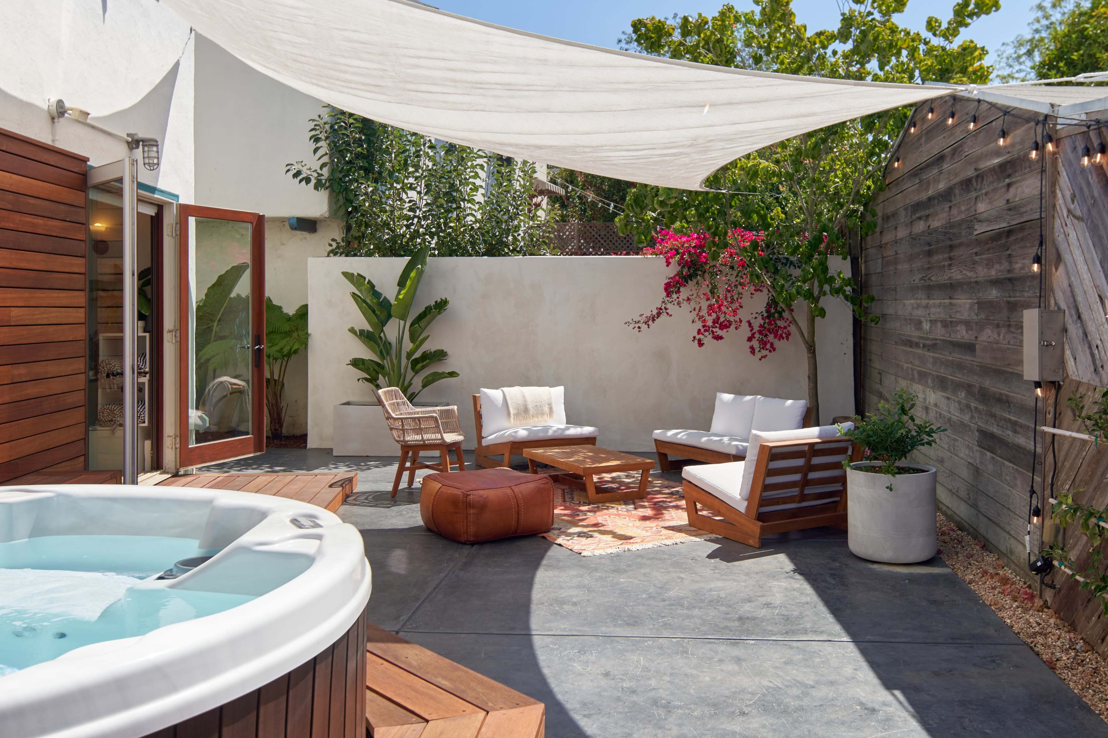 A private outdoor patio features a hot tub, comfortable seating, and decorative plants under a shaded canopy.