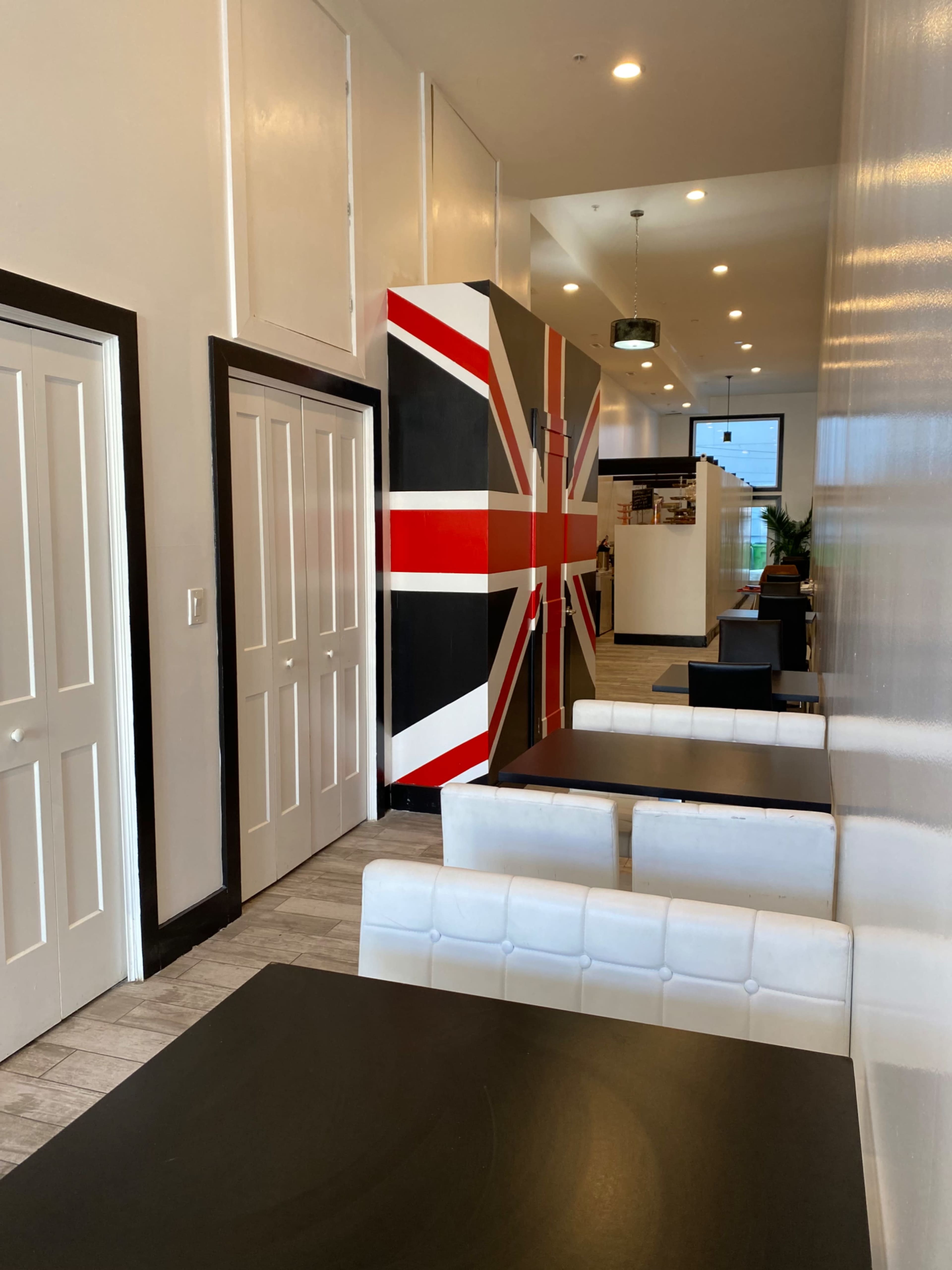 A narrow corridor in a restaurant featuring a large mural of the Union Jack on the wall, flanked by white seating areas and doors leading to other rooms.